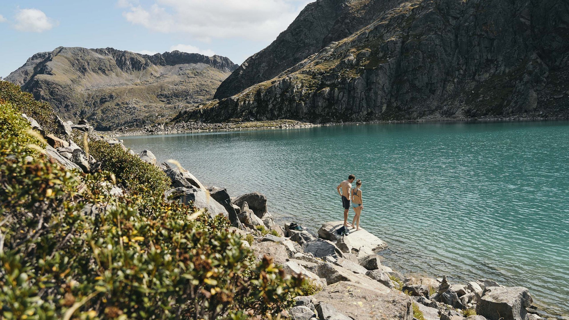 Things to do in Stubaital Two people standing by a mountain lake shore with rocks and mountains nearby