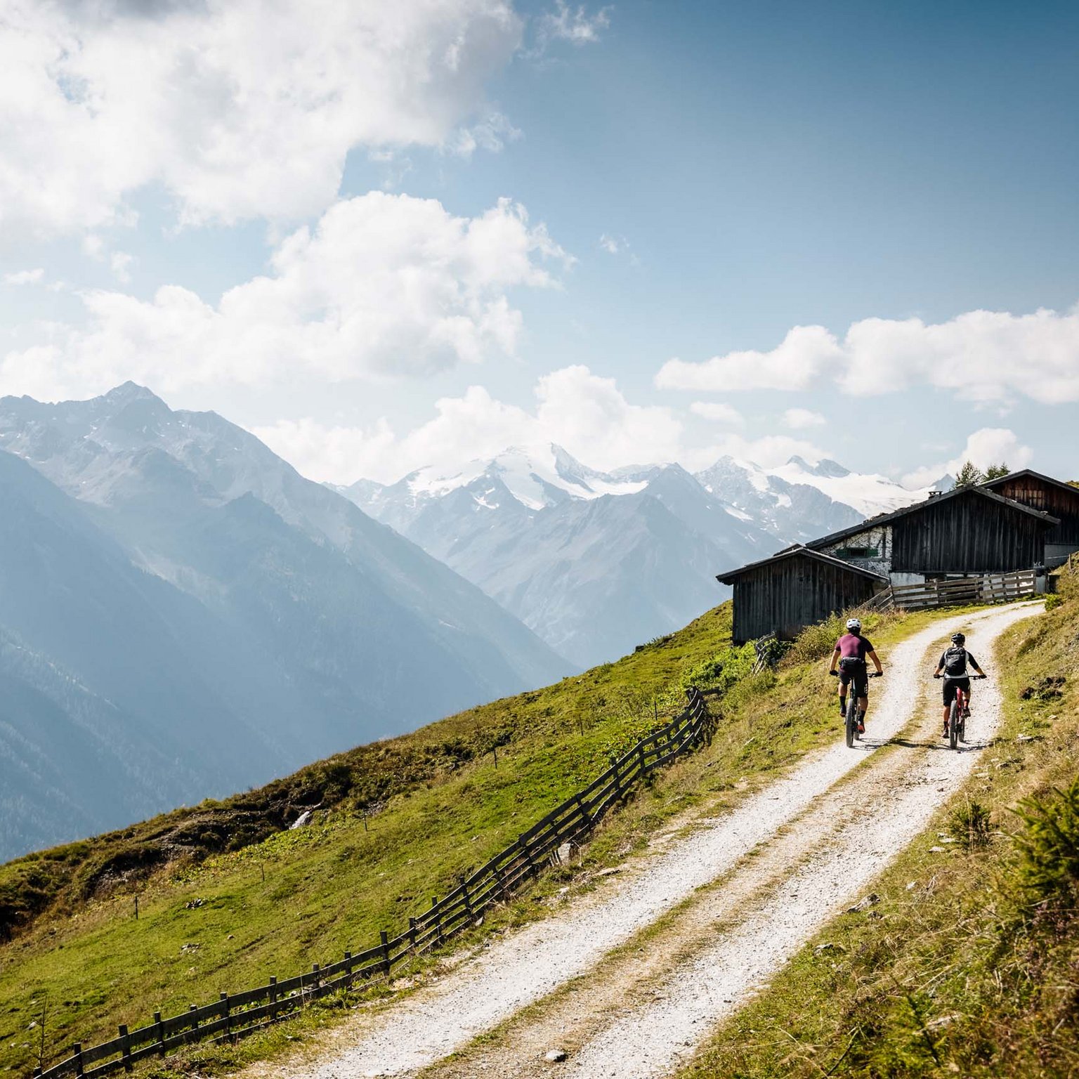 Stubaital: Hiking in summer Two cyclists on mountain path with alpine scenery and huts in the background