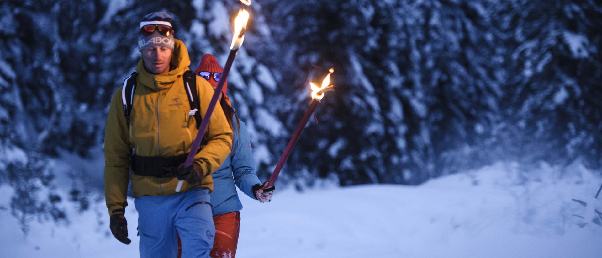 Das Event in Neustift Klaus Äuele Zwei Personen wandern mit Fackeln durch verschneiten Wald im Abendlicht