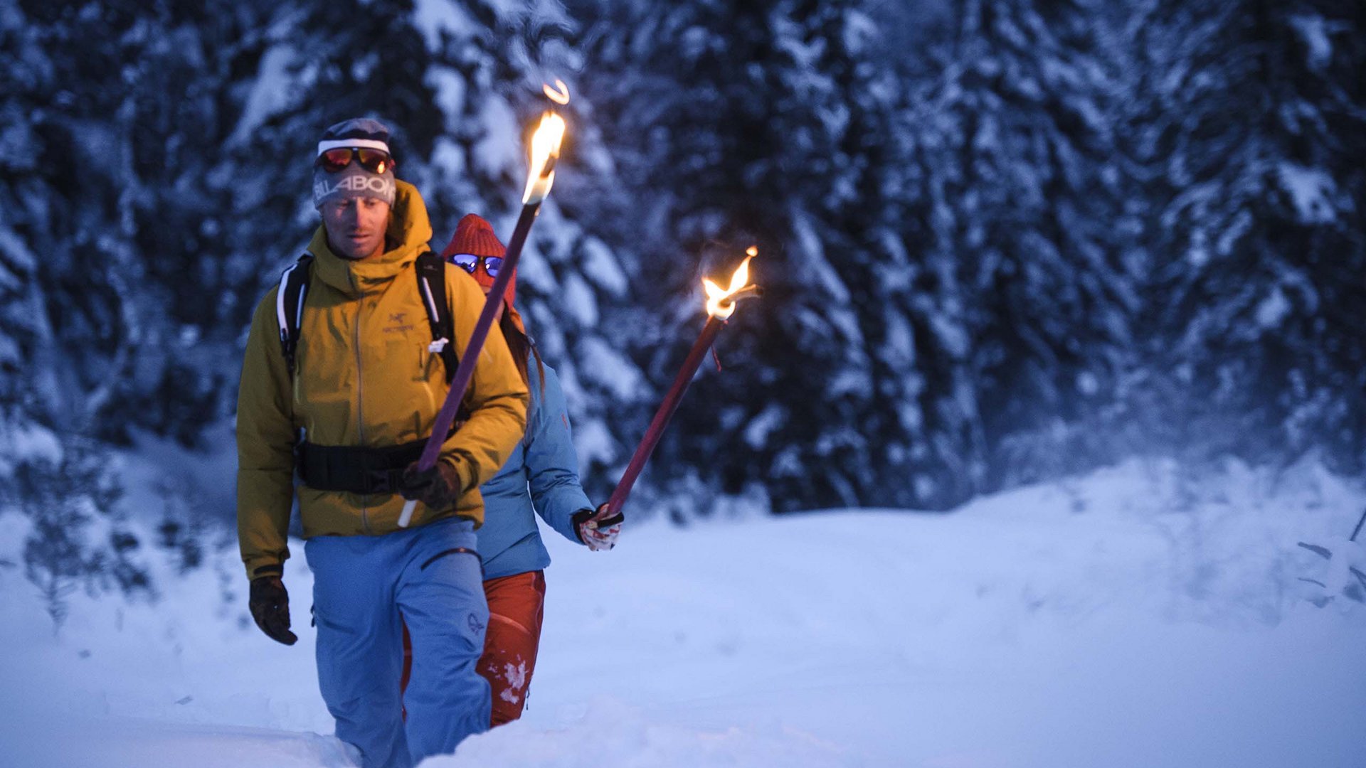 Neustift: the active hotel in Stubaital Two people walking with torches in a snowy forest at dusk