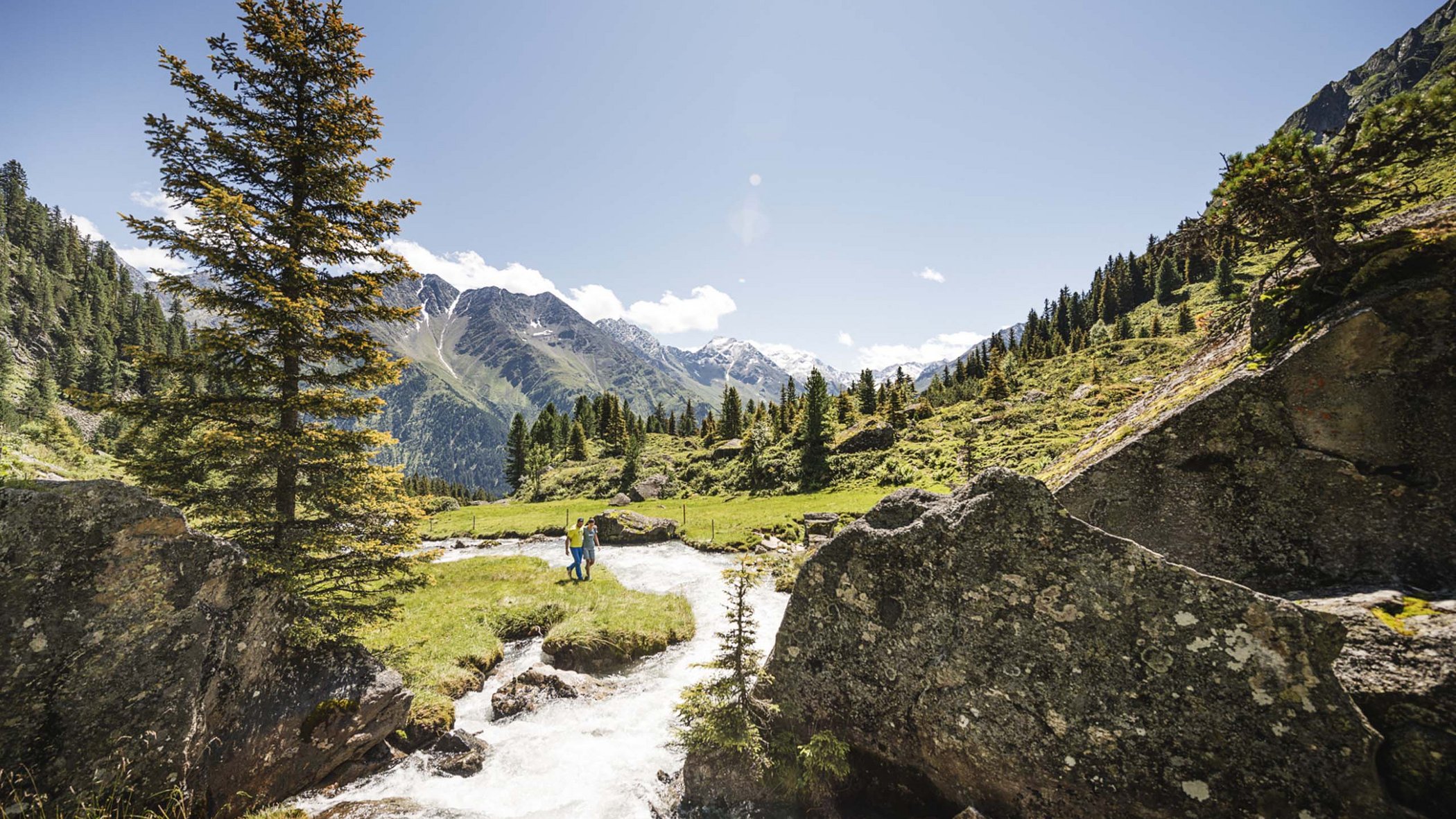 Stubaital: Hiking in summer Mountain landscape with river, trees, and people on a green meadow