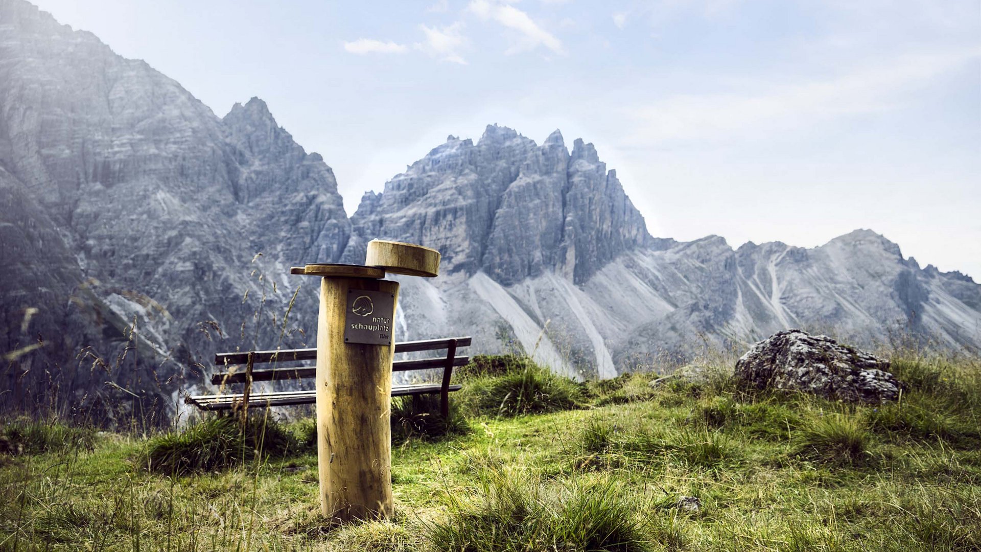 In Stubaital ci son mille cose da fare Palo di legno con panca davanti a montagne rocciose e prato