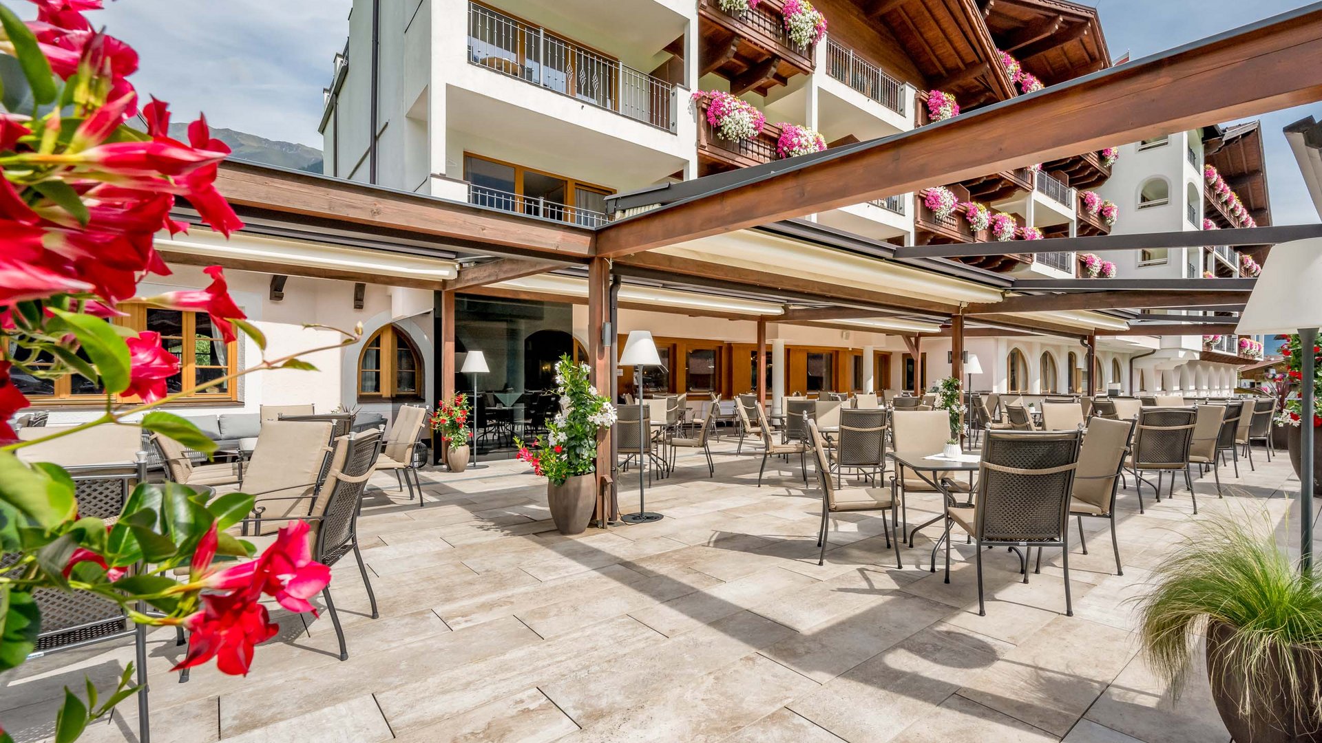 Stubaital: our hotel with a pool Terrace with outdoor seating and flowers on hotel balconies
