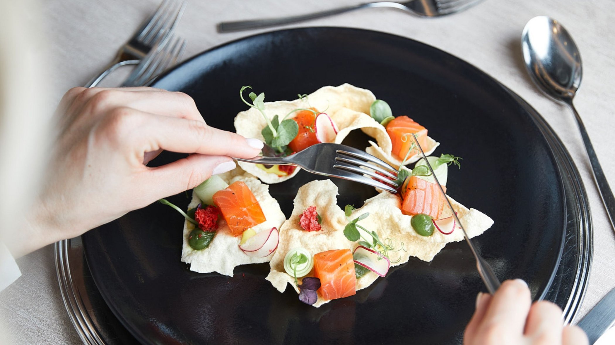 Vacanze in Tirolo all’insegna del gusto Persona mangia piatto gourmet con salmone e decorazioni su piatto nero