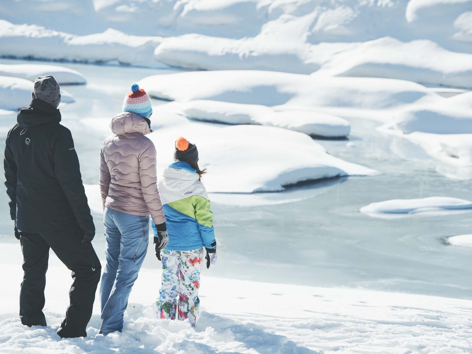 Stubaital: our hotel with a pool Three people in winter clothes stand on snow looking at a frozen lake