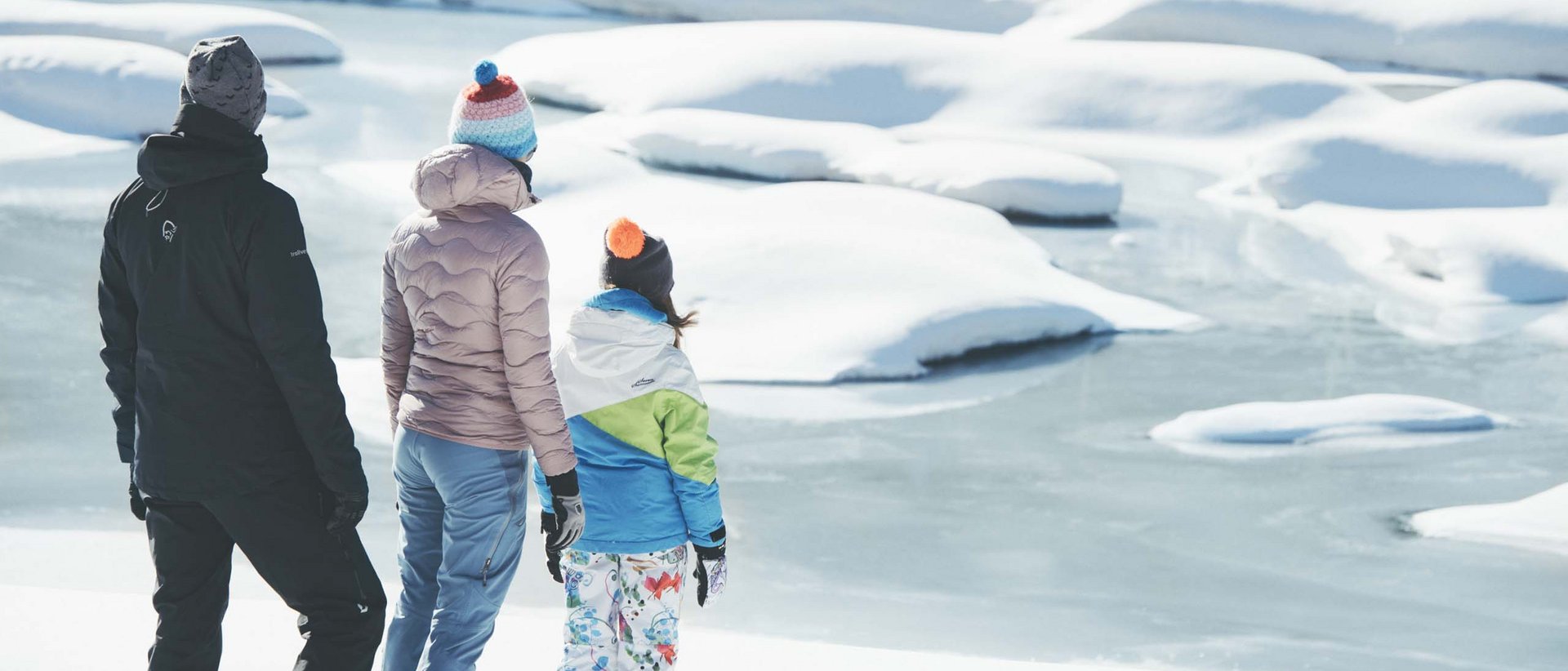 Hier ist was los! Drei Personen in Winterkleidung stehen im Schnee und blicken auf einen zugefrorenen See