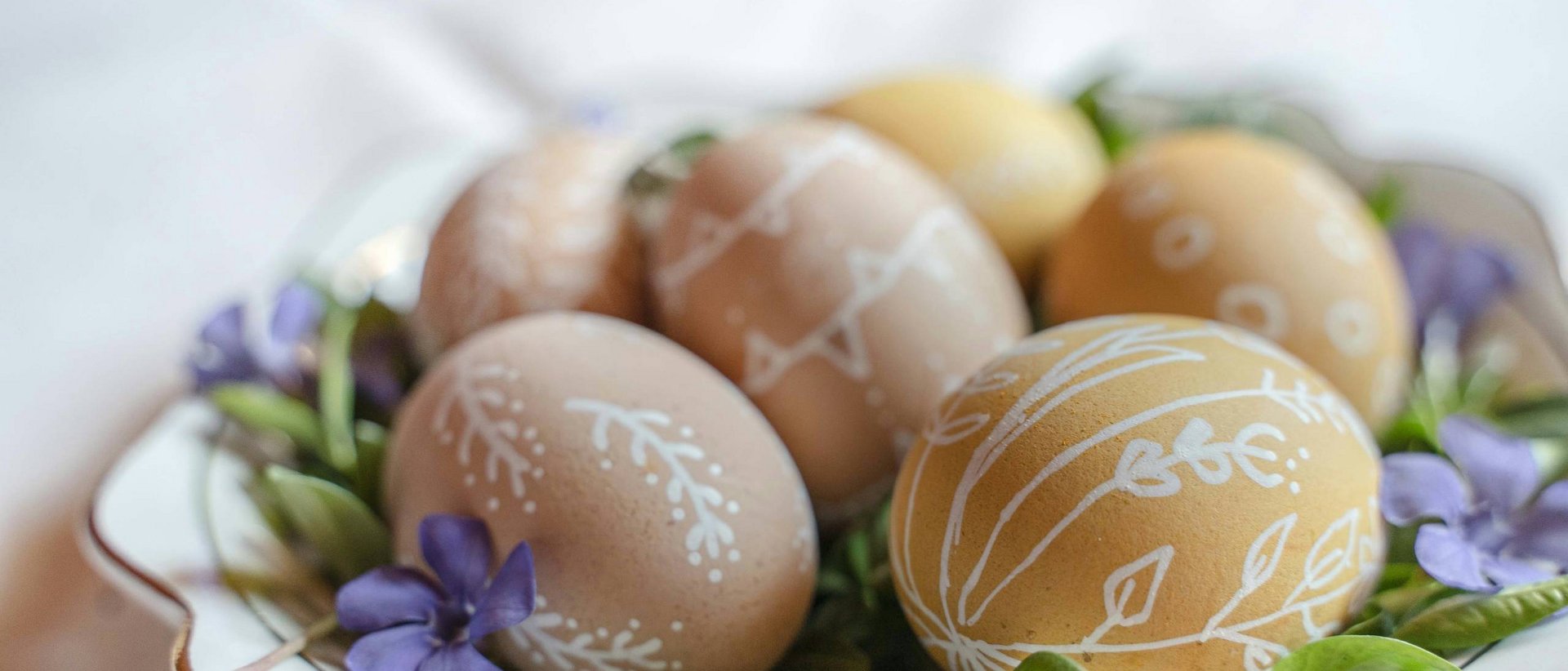 Ostern steht vor der Tür! Ostereier mit weißen Mustern auf einem Teller mit grünen Blättern und lila Blumen