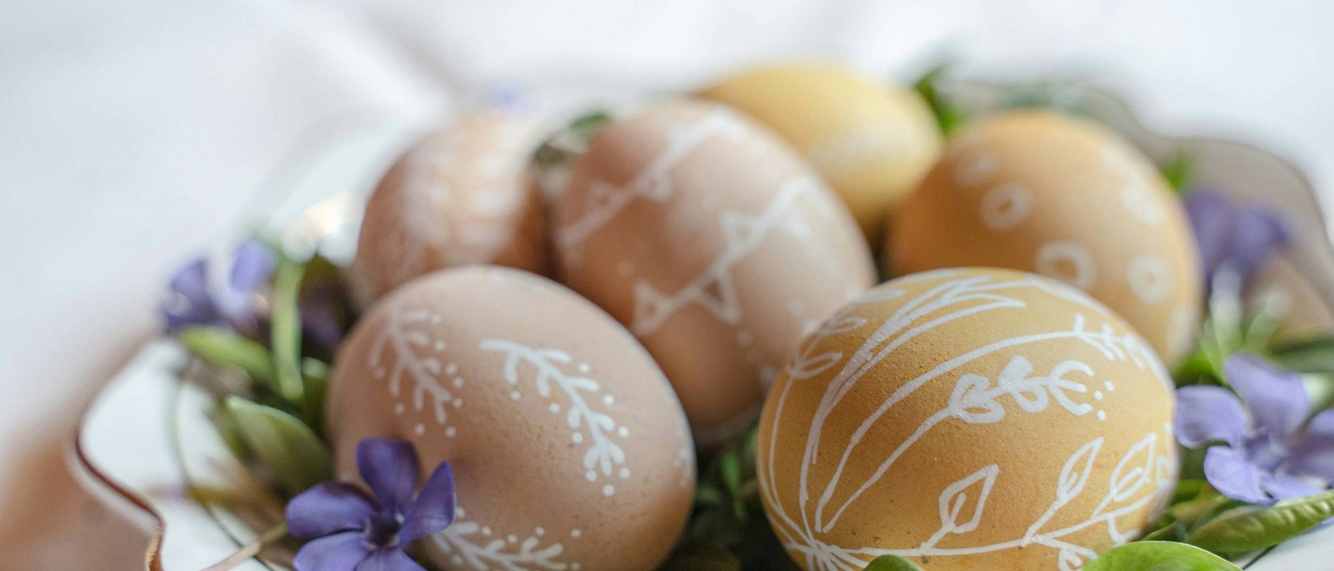Ostern steht vor der Tür! Ostereier mit weißen Mustern auf einem Teller mit grünen Blättern und lila Blumen