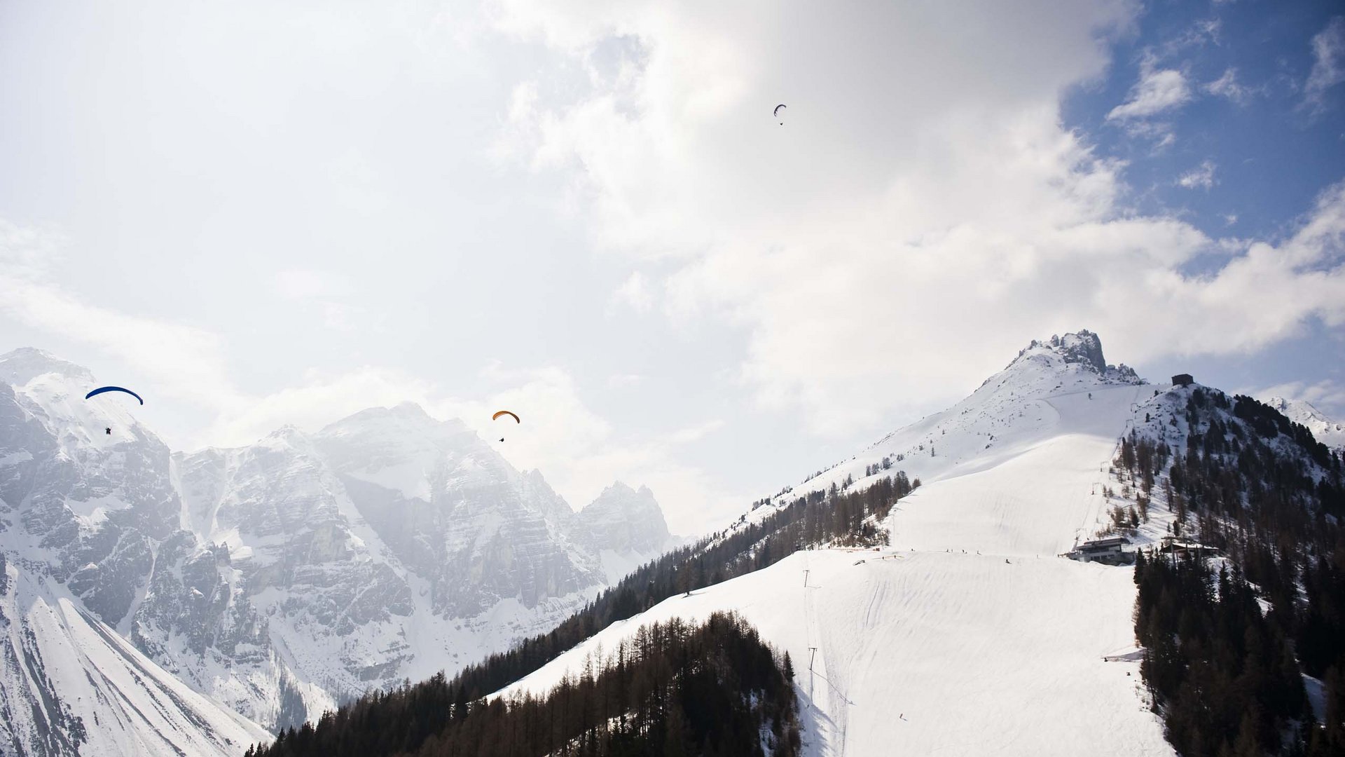 Neustift: the active hotel in Stubaital Three paragliders flying over snowy mountains and forest
