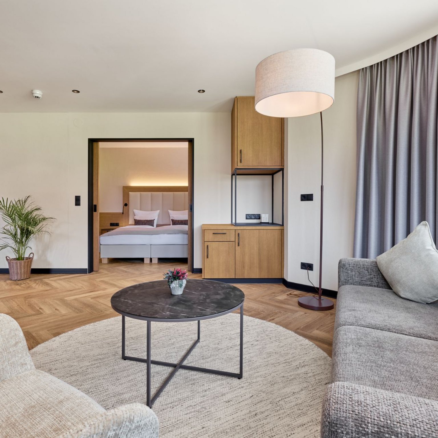 Neustift: Hotel zum Wohlfühlen Helles Wohnzimmer mit grauem Sofa, Beistelltisch und Blick ins Schlafzimmer