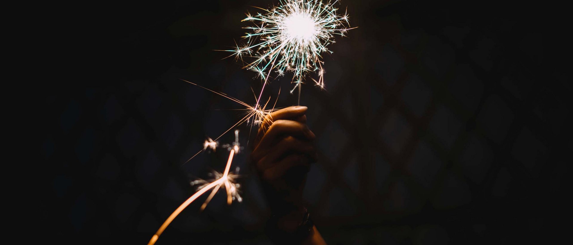 Bye 2024, willkommen 2025! Hand hält helle Wunderkerze im Dunkeln