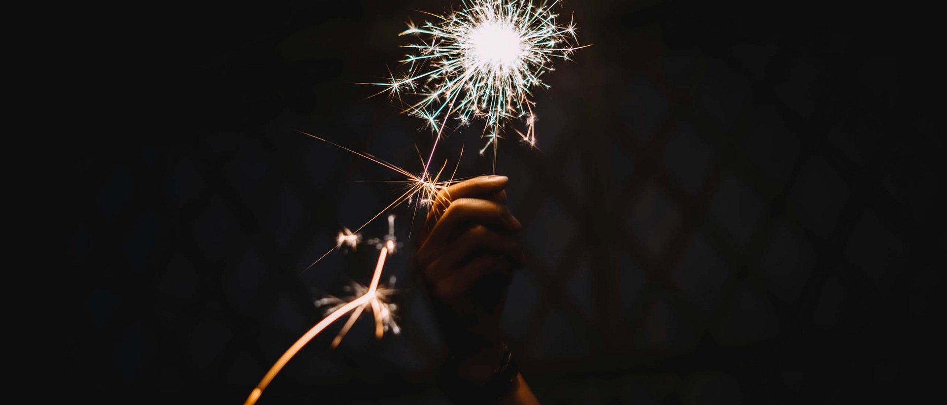 Bye 2024, willkommen 2025! Hand hält helle Wunderkerze im Dunkeln