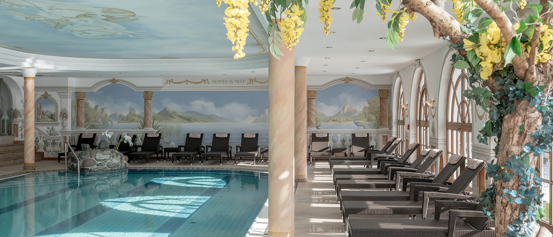 Ihr Wellnessurlaub im Milderer Hof Innenpool mit Liegestühlen und Wandgemälden in einem luxuriösen Spa
