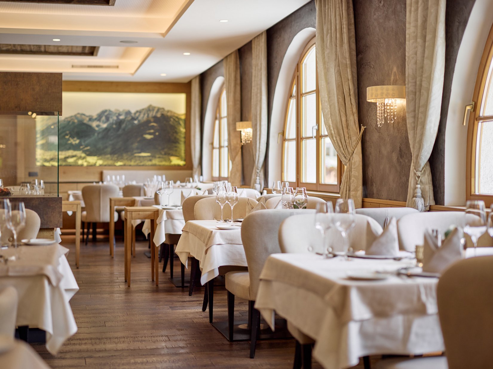 Stubaital: our hotel with a pool Elegant restaurant with white tablecloths and mountain painting on the wall