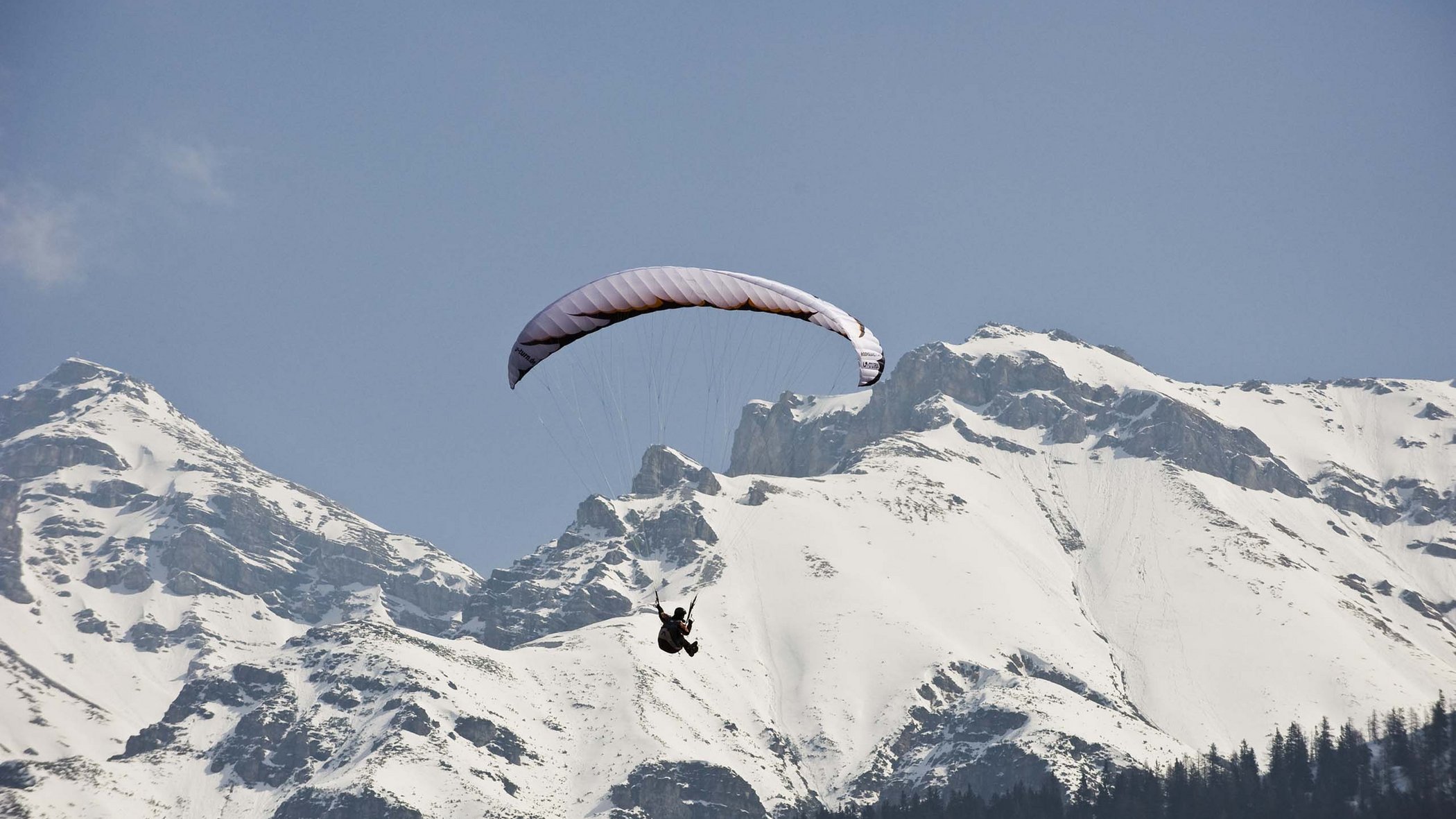 Langlaufen im Stubaital und mehr Paragleiter fliegt vor schneebedeckten Bergen unter blauem Himmel