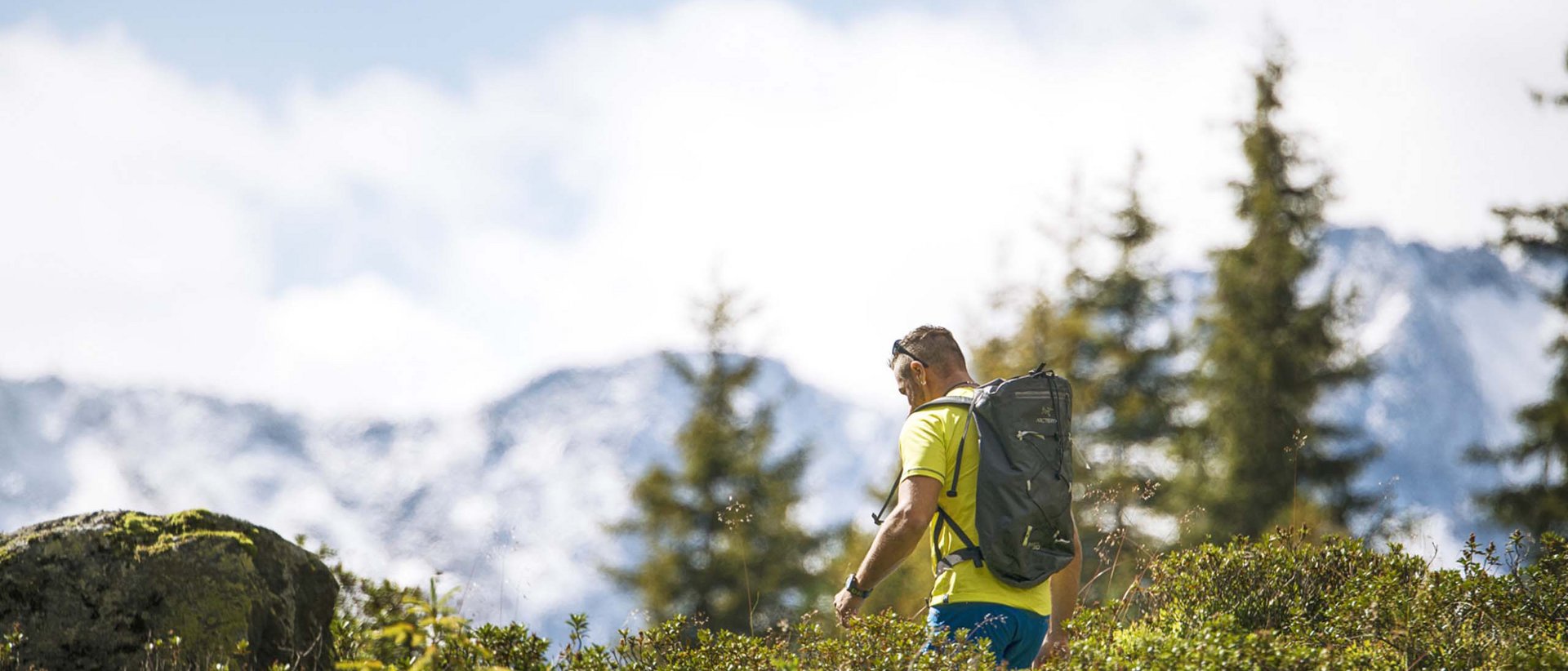 Höher, schneller, weiter Wanderer mit Rucksack in grüner Berglandschaft vor schneebedeckten Gipfeln