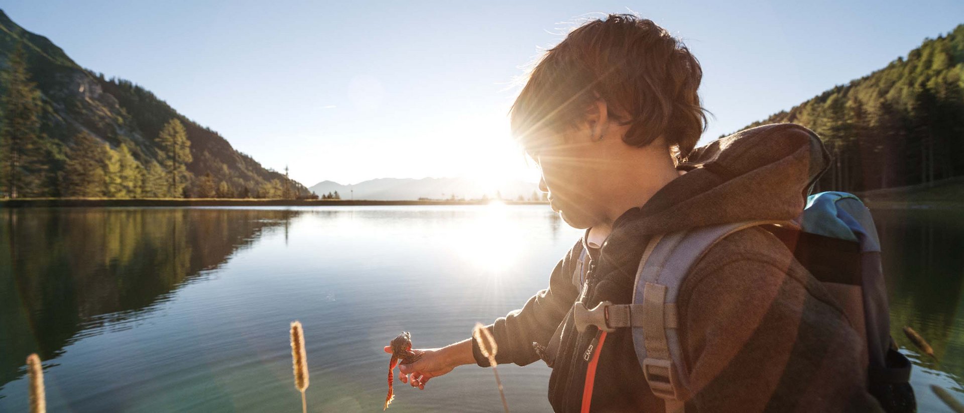 Ein fabelhafter Familiensommer Junge am See hält Seil mit Anhänger in der Hand bei Sonnenuntergang