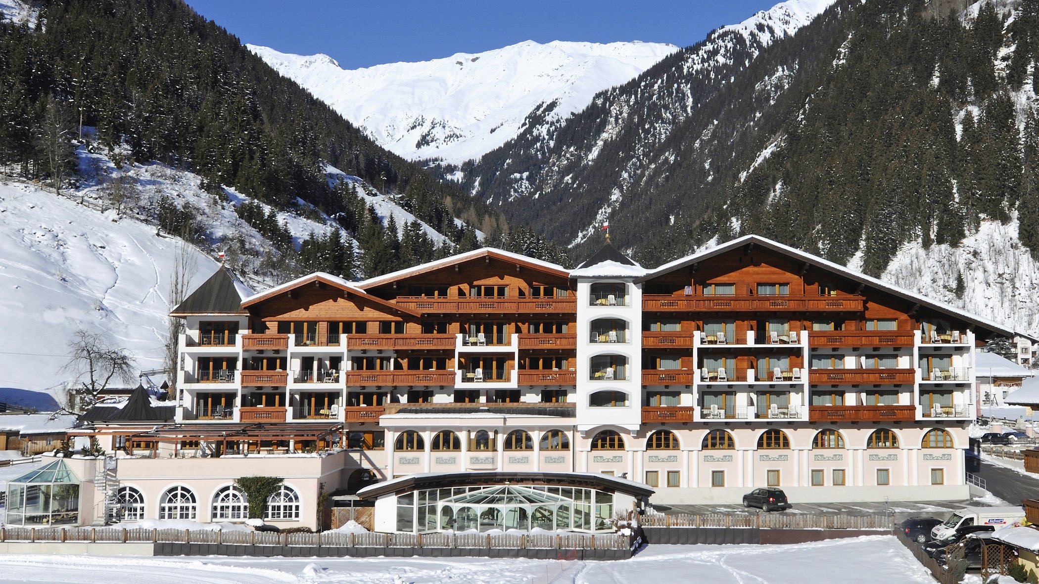 Ecco il nostro hotel: lo Stubai vi aspetta Grande hotel in valle innevata con montagne boschive e cielo azzurro