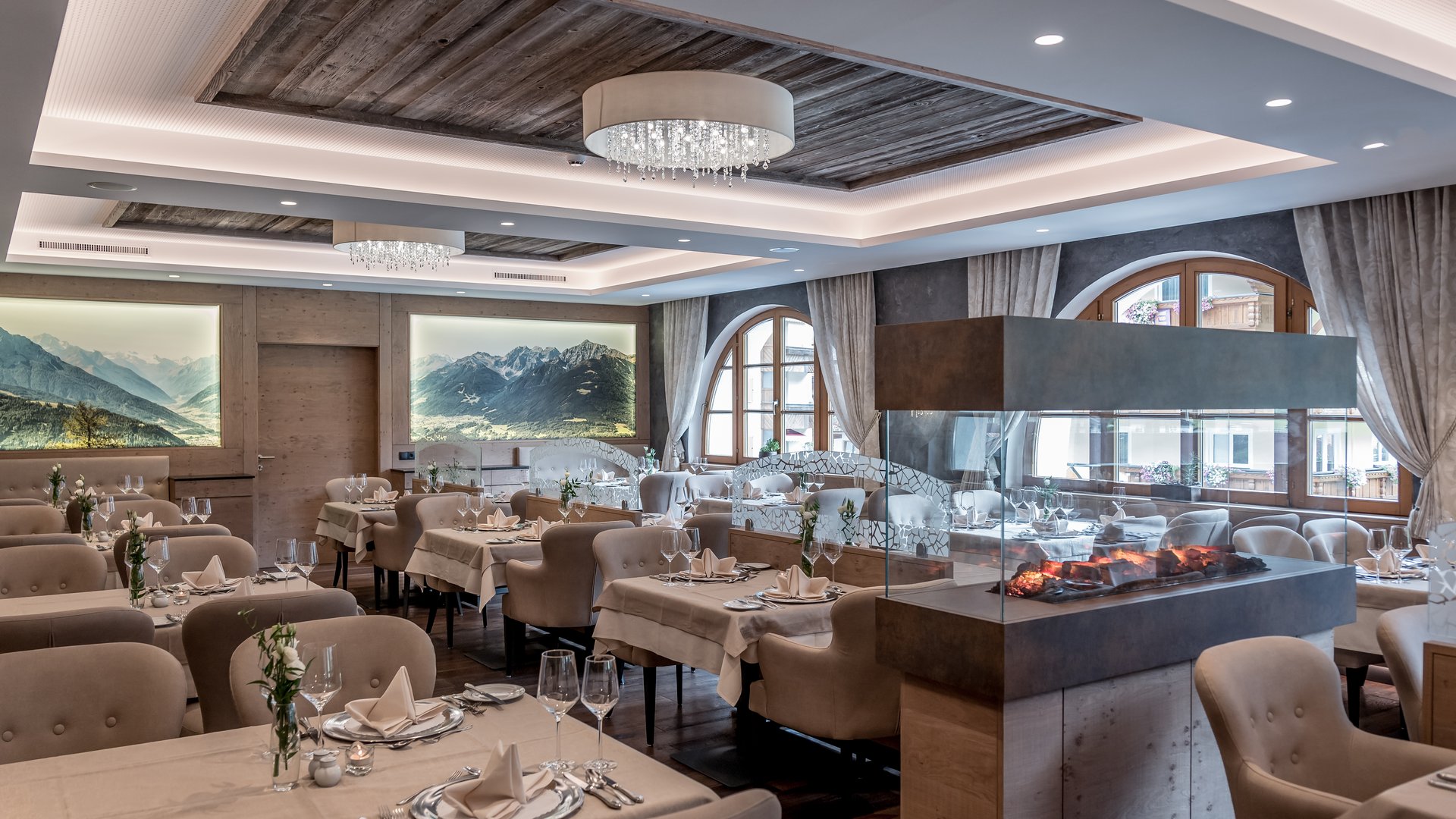 Stubaital: our hotel with a pool Elegant restaurant with fireplace, set tables, and mountain paintings on walls