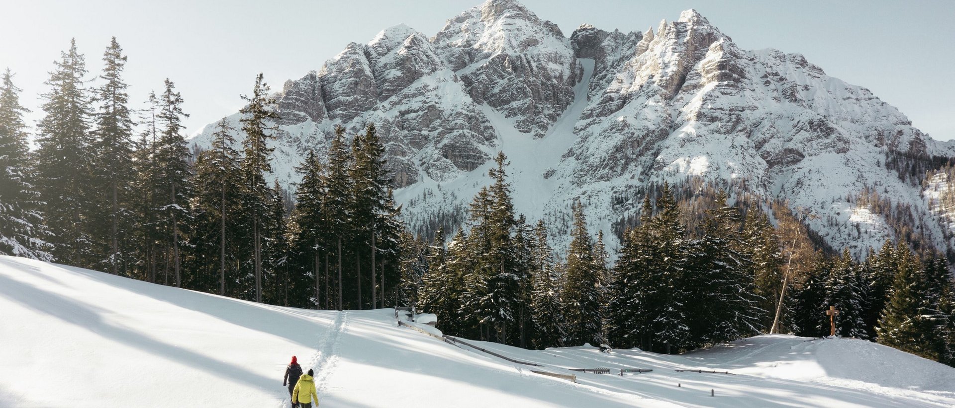 Winterurlaub im Stubaital: Warum die Berge uns sofort entschleunigen Zwei Personen wandern durch verschneite Landschaft mit Tannen und Berg im Hintergrund