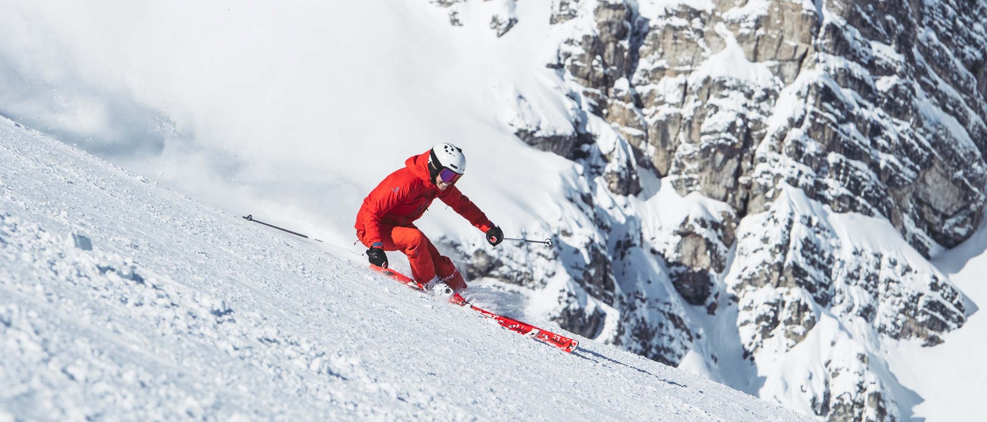 Die Skisaison beginnt bald! Skifahrer in roter Kleidung fährt bergab auf verschneiter Piste vor Felsen