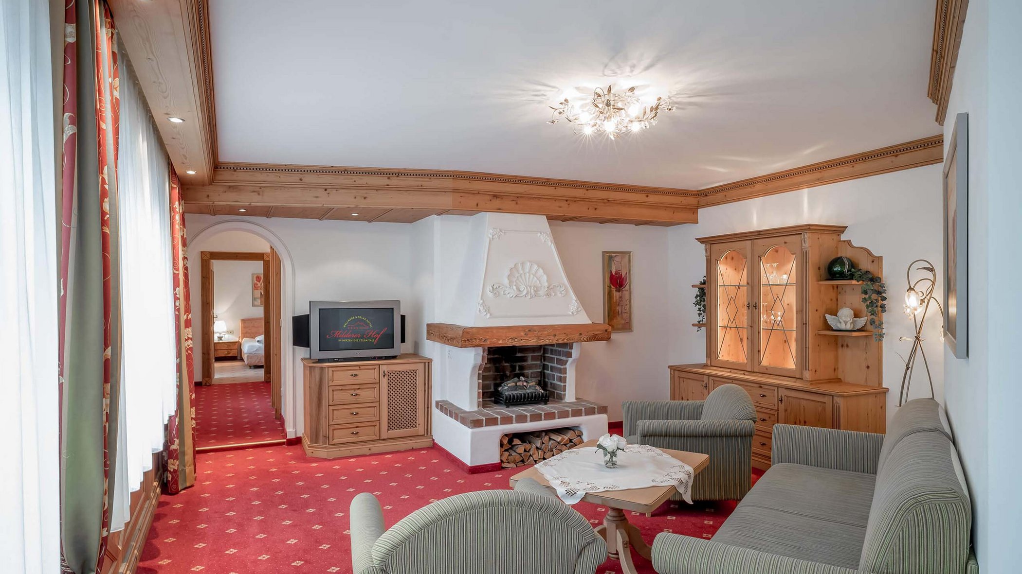 Neustift: Hotel zum Wohlfühlen Wohnzimmer mit Kamin, TV, Holzmöbeln und rotem Teppich