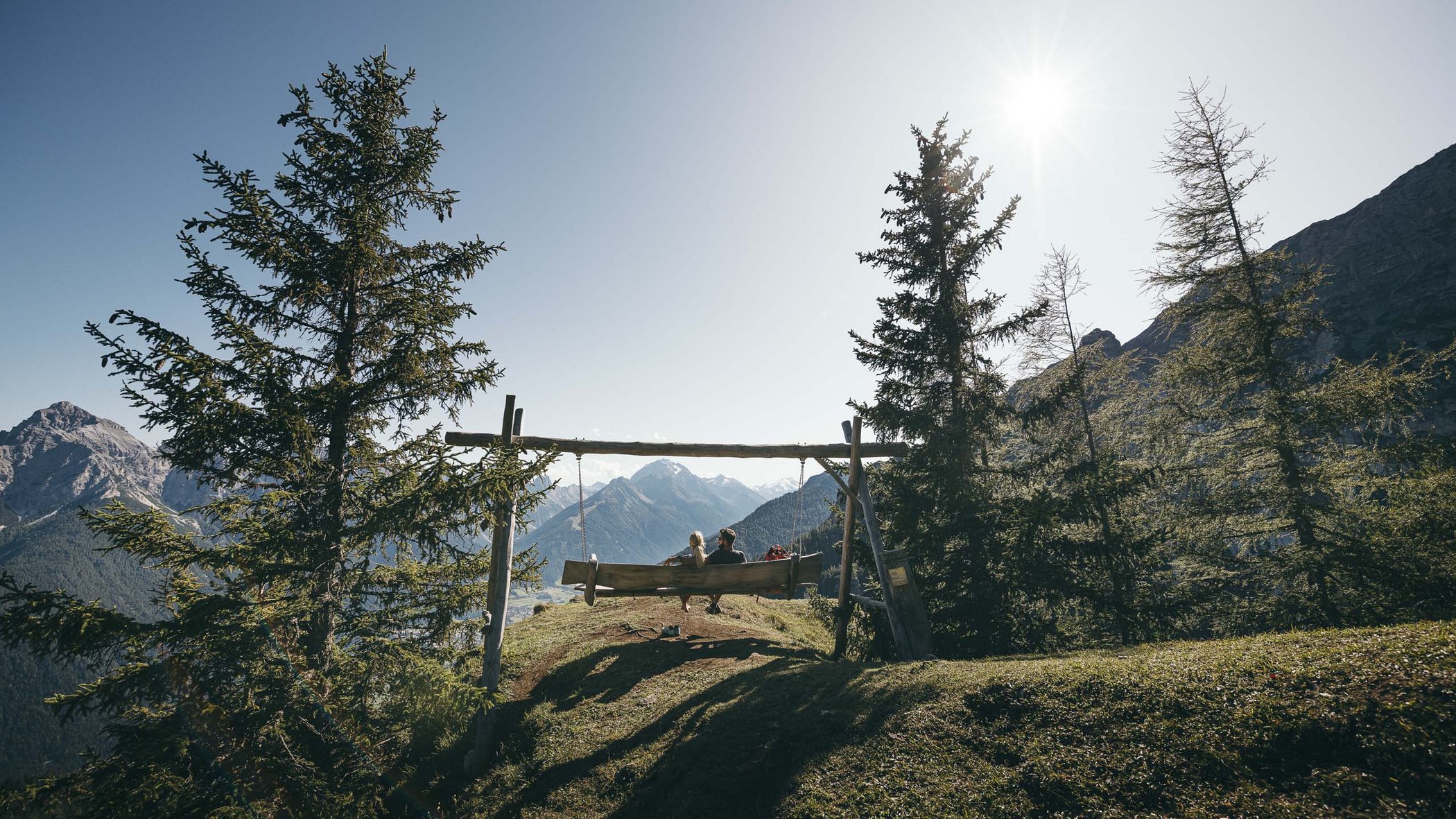 Rund um den Gletscher: Tirol im Sommer Paar sitzt auf Holzschaukel mit Bergpanorama bei Sonnenschein