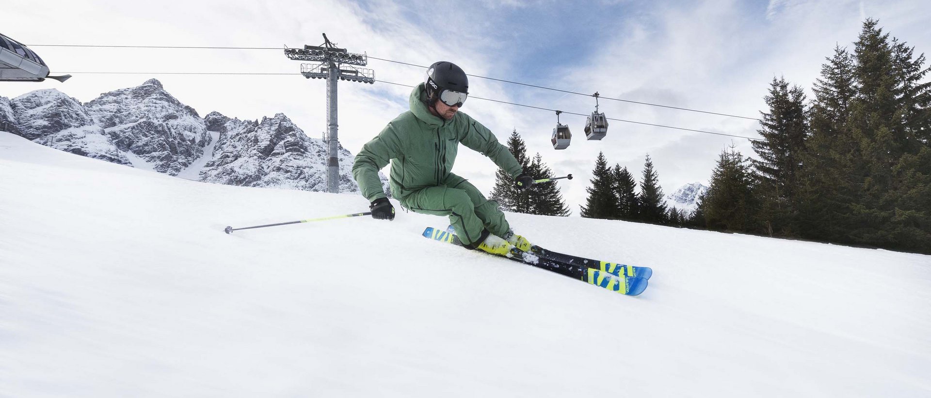 Noch mehr Platz für Ihre Skier Skifahrer in grüner Kleidung fährt eine Piste mit Berglandschaft und Gondeln im Hintergrund