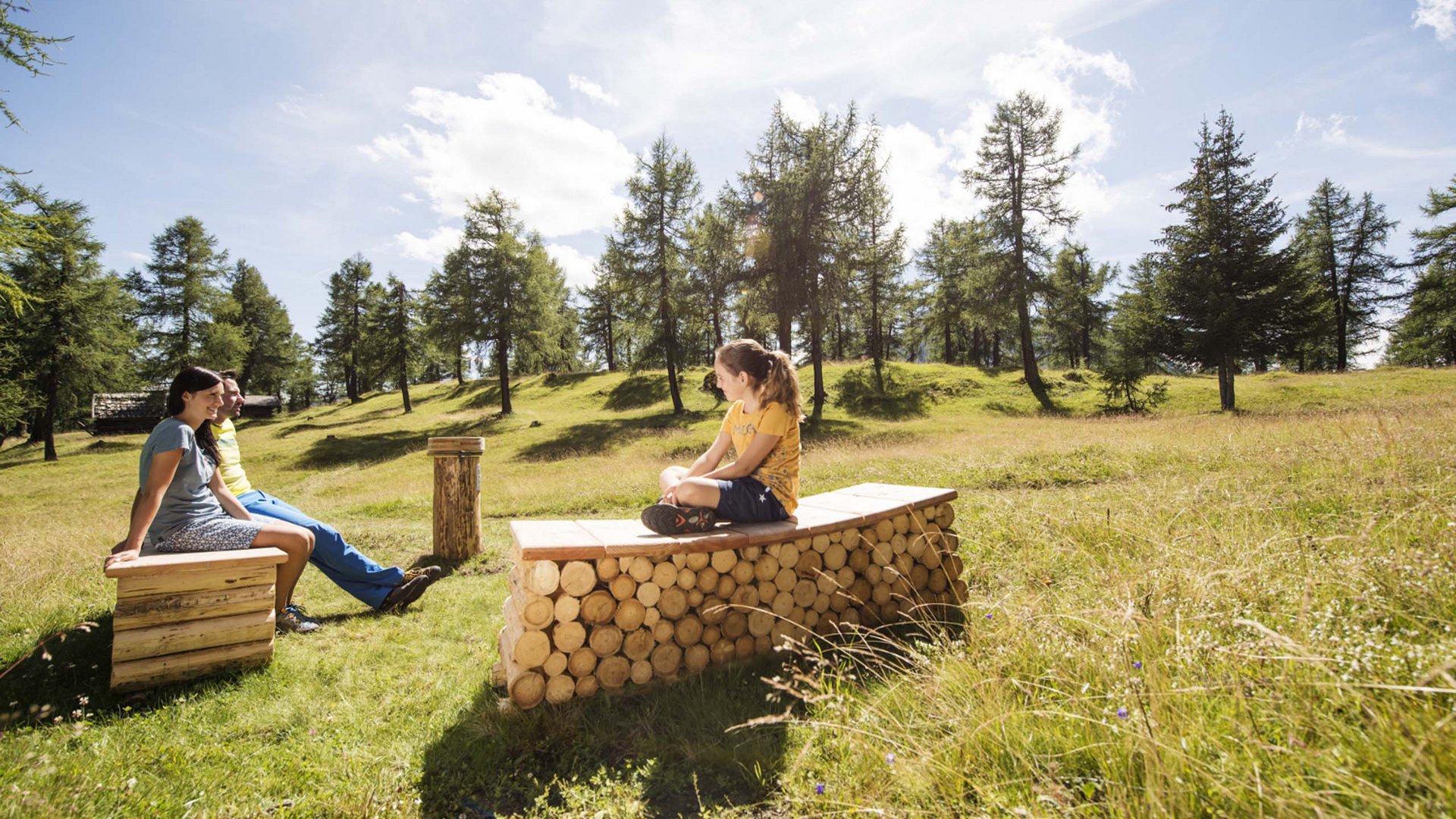 In Stubaital ci son mille cose da fare Famiglia seduta su panchine di legno in radura soleggiata con prato verde