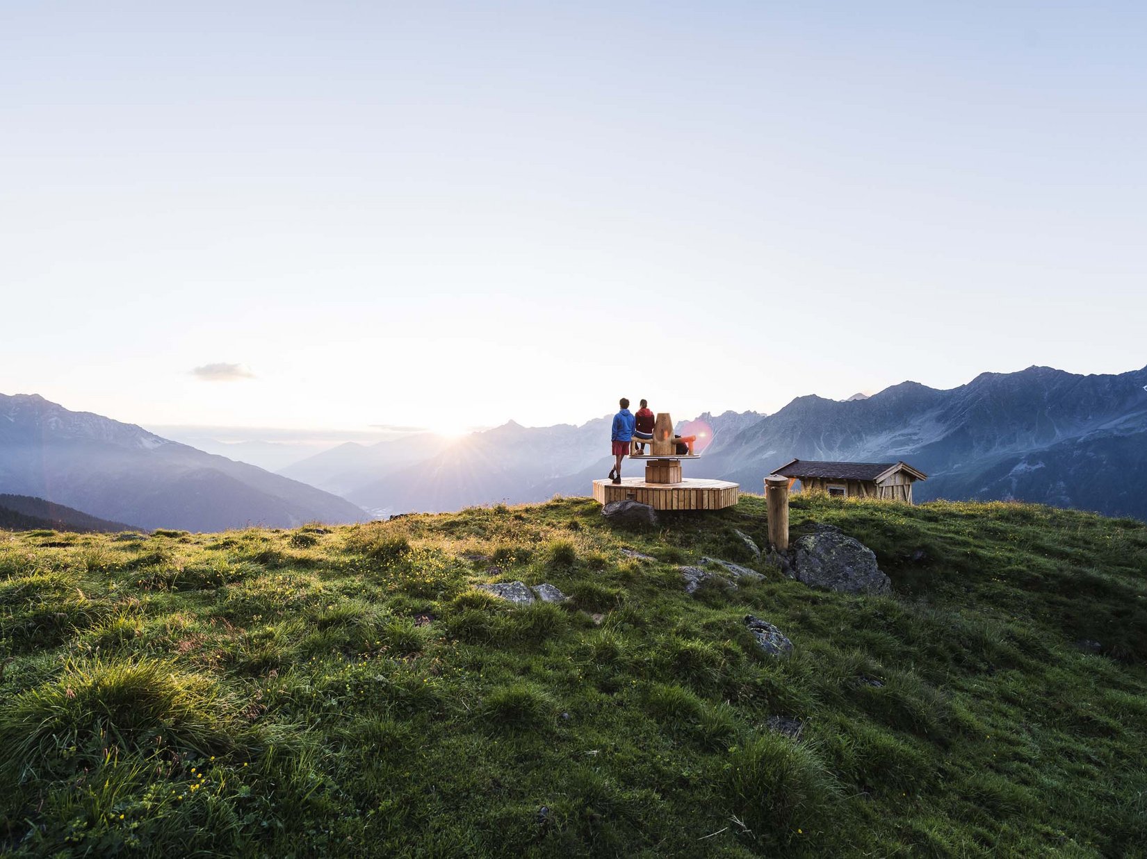 Stubaital: our hotel with a pool Two people on a wooden platform in the mountains at sunset