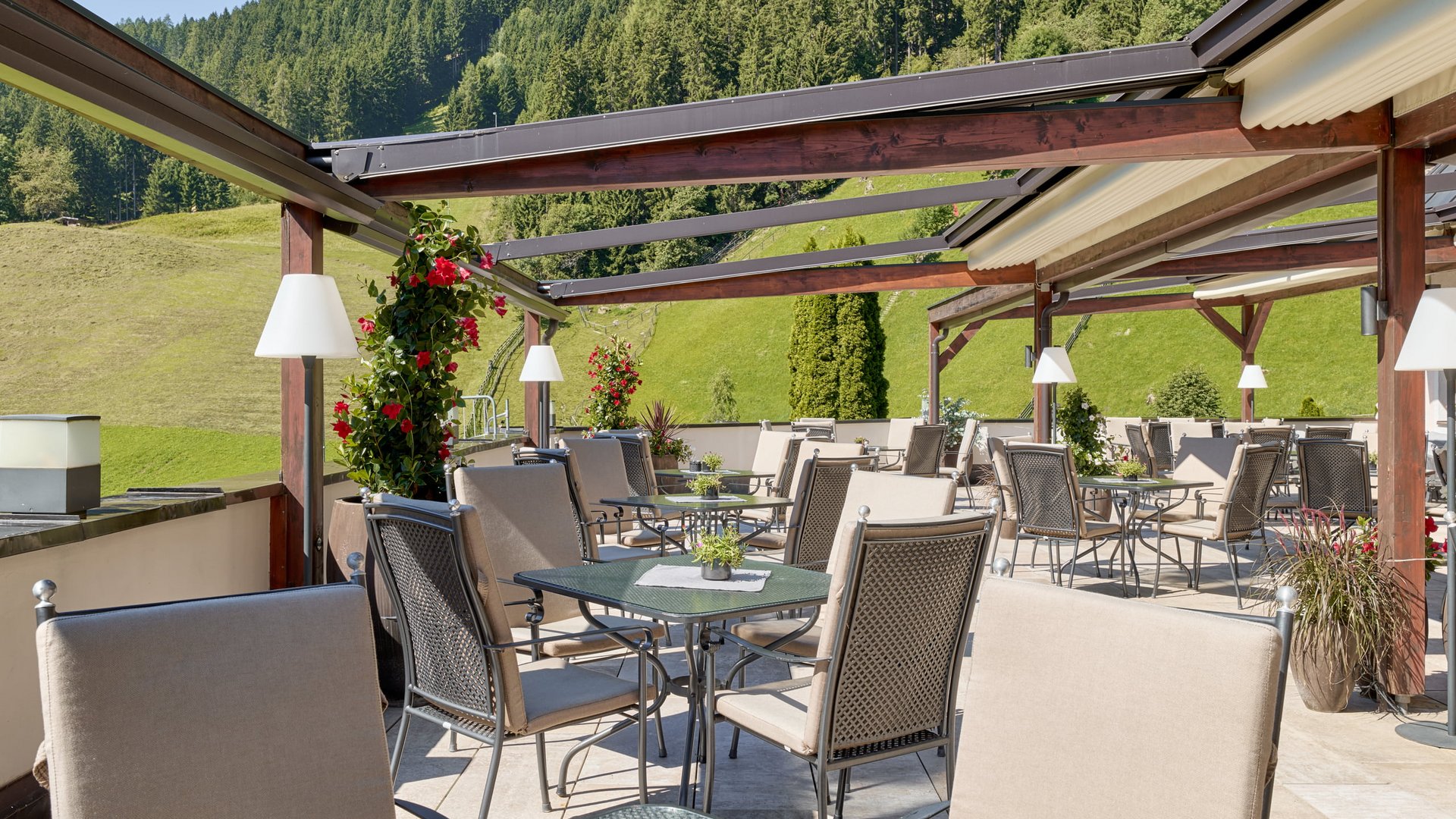 Stubaital: our hotel with a pool Terrace with chairs and tables overlooking wooded hillside in sunlight
