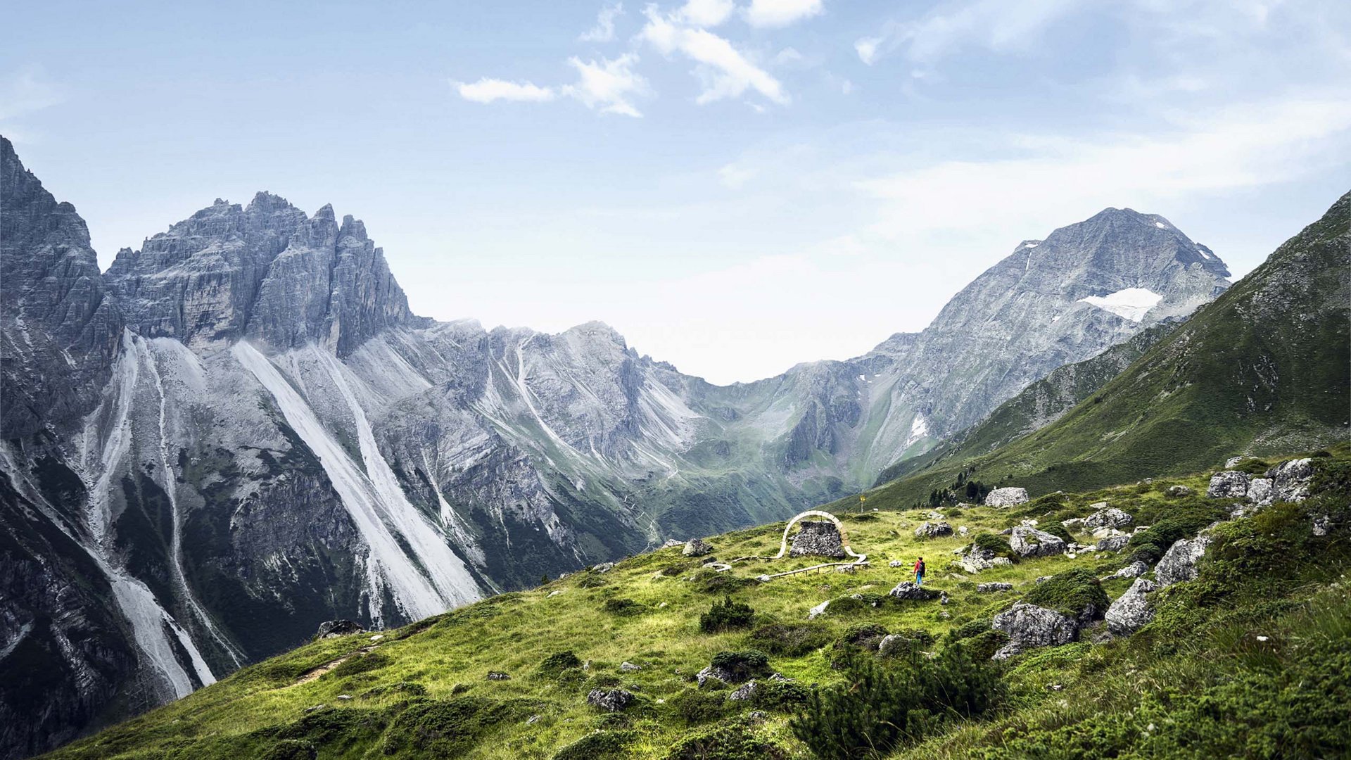 Rund um den Gletscher: Tirol im Sommer Grüne Bergwiese mit felsigen Gipfeln und einer kleinen Steinskulptur unter blauem Himmel