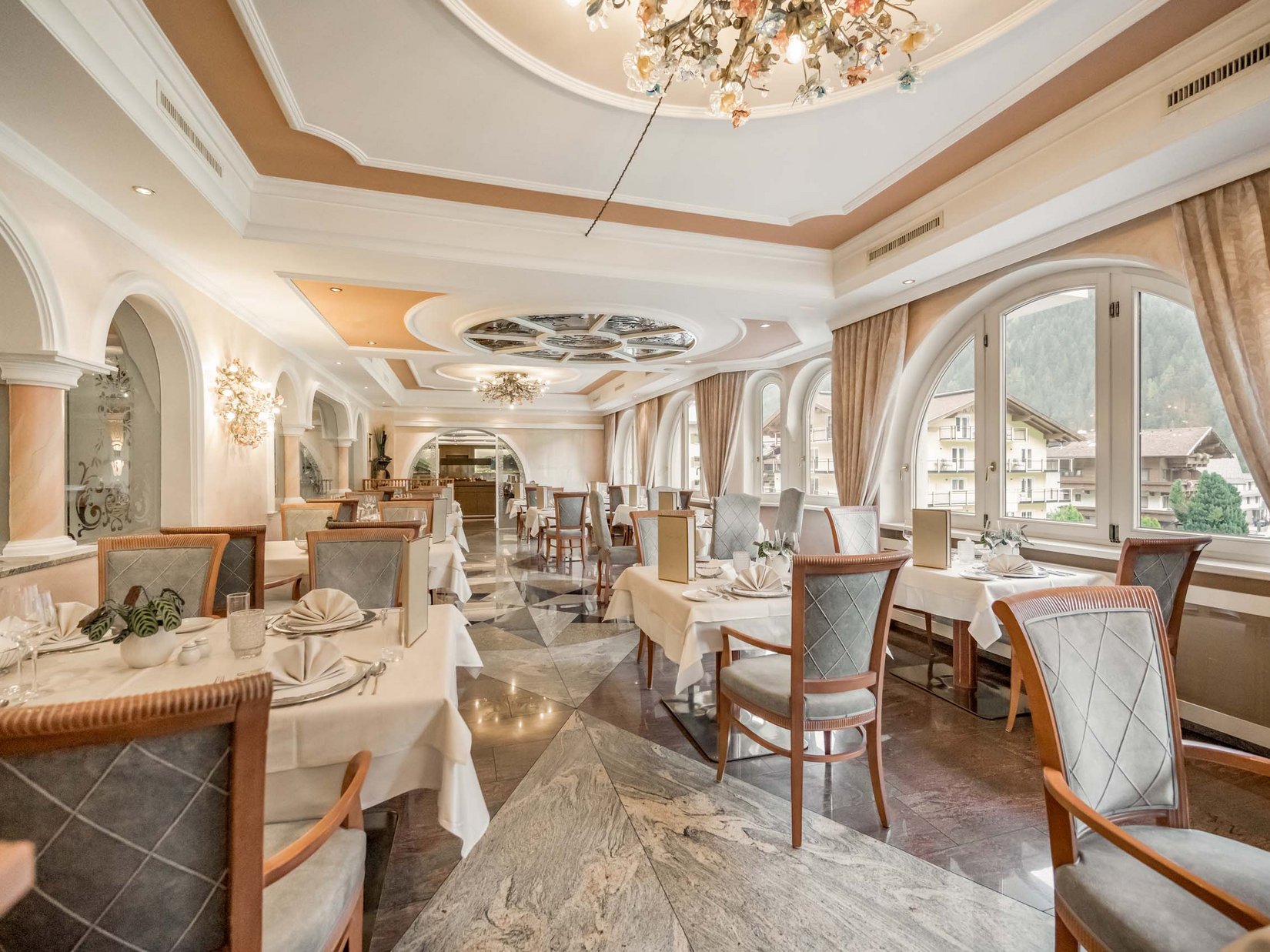 Stubaital: our hotel with a pool Elegant restaurant with set tables and large windows overlooking mountain view