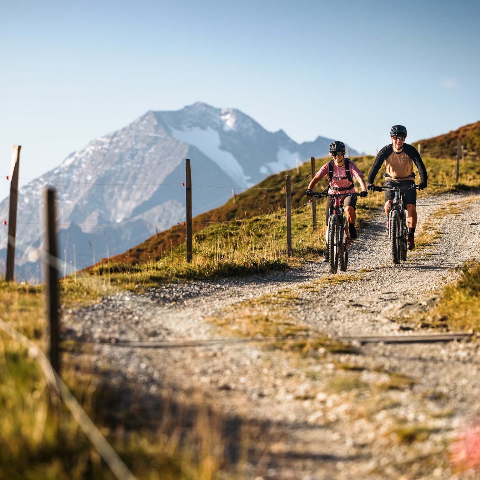Stubaital: our hotel with a pool Two mountain bikers cycling on a mountain trail with snowy peak in the background