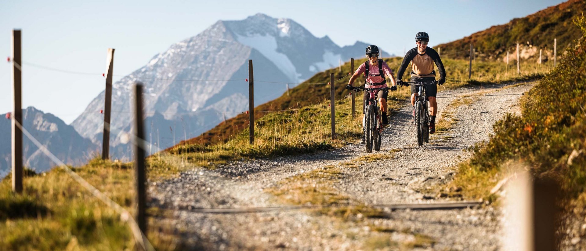 Ein aussichtsreiches Sporterlebnis Zwei Mountainbiker fahren auf einem Bergweg mit schneebedecktem Gipfel im Hintergrund