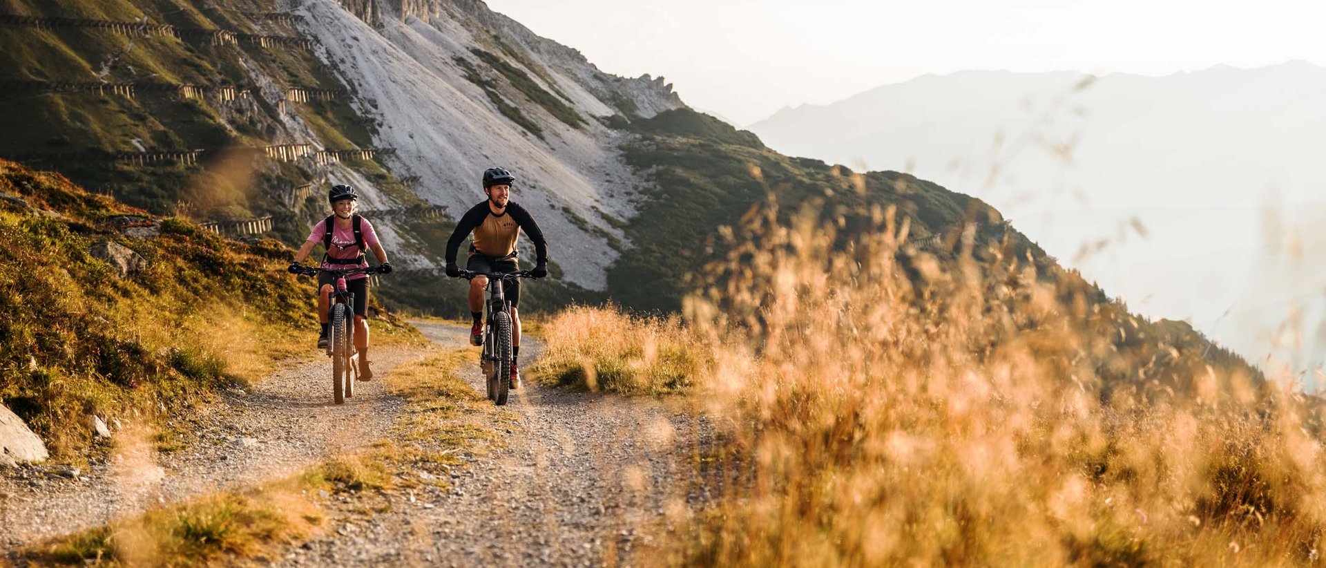 So vielseitig ist der Herbst im Stubaital. Zwei Mountainbiker fahren auf Bergweg mit Felsen im Hintergrund bei Sonnenlicht