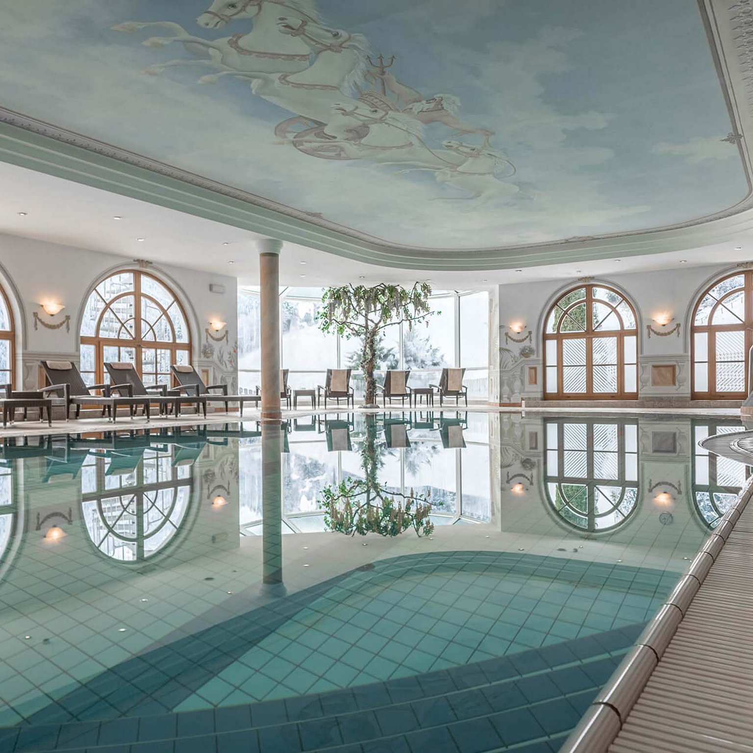 Stubaital: our hotel with a pool Indoor pool with lounge chairs and large windows in an elegant room