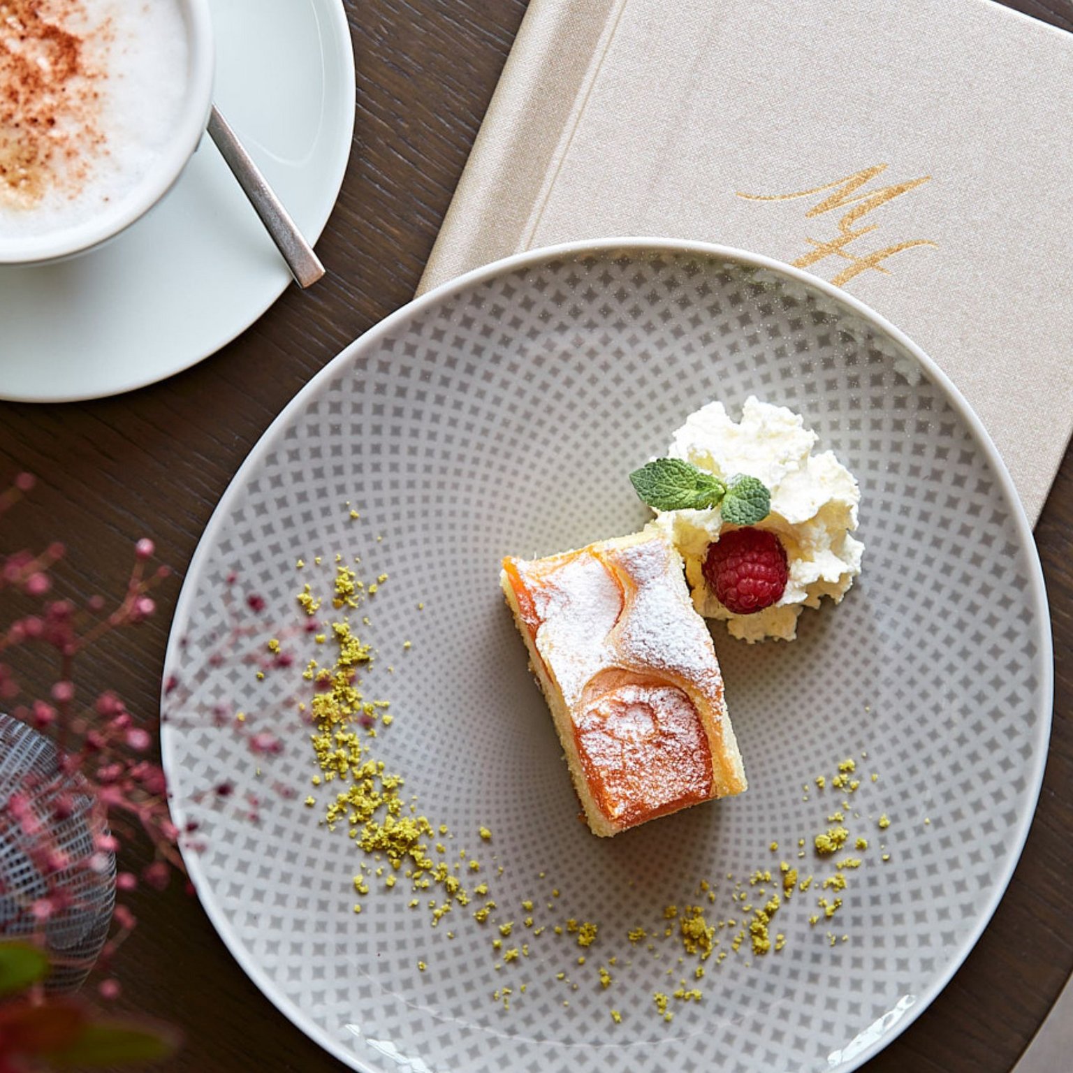 Vacanze in Tirolo all’insegna del gusto Una fetta di torta con panna e lampone su un piatto accanto a un cappuccino