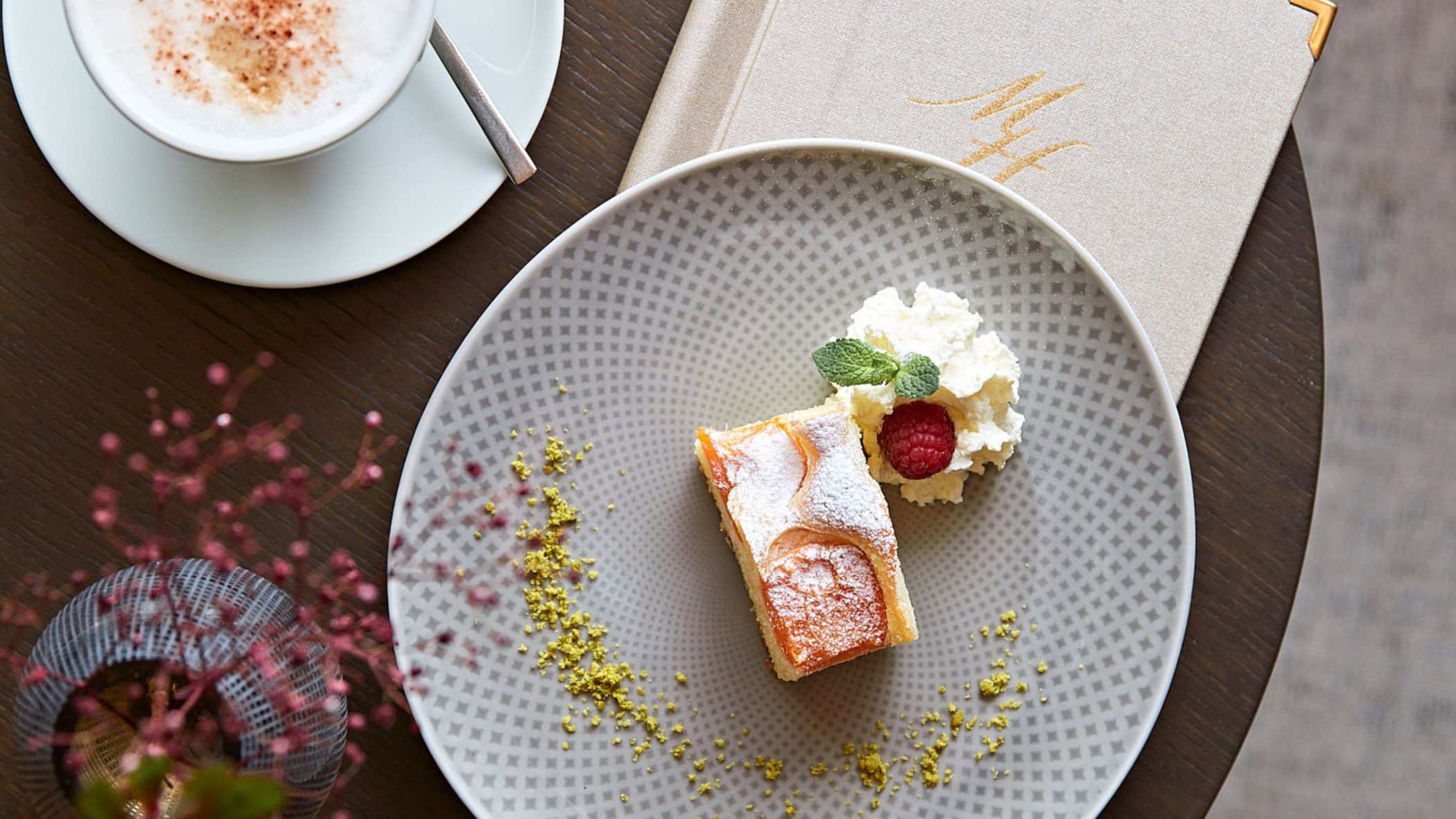 Vacanze in Tirolo all’insegna del gusto Una fetta di torta con panna e lampone su un piatto accanto a un cappuccino