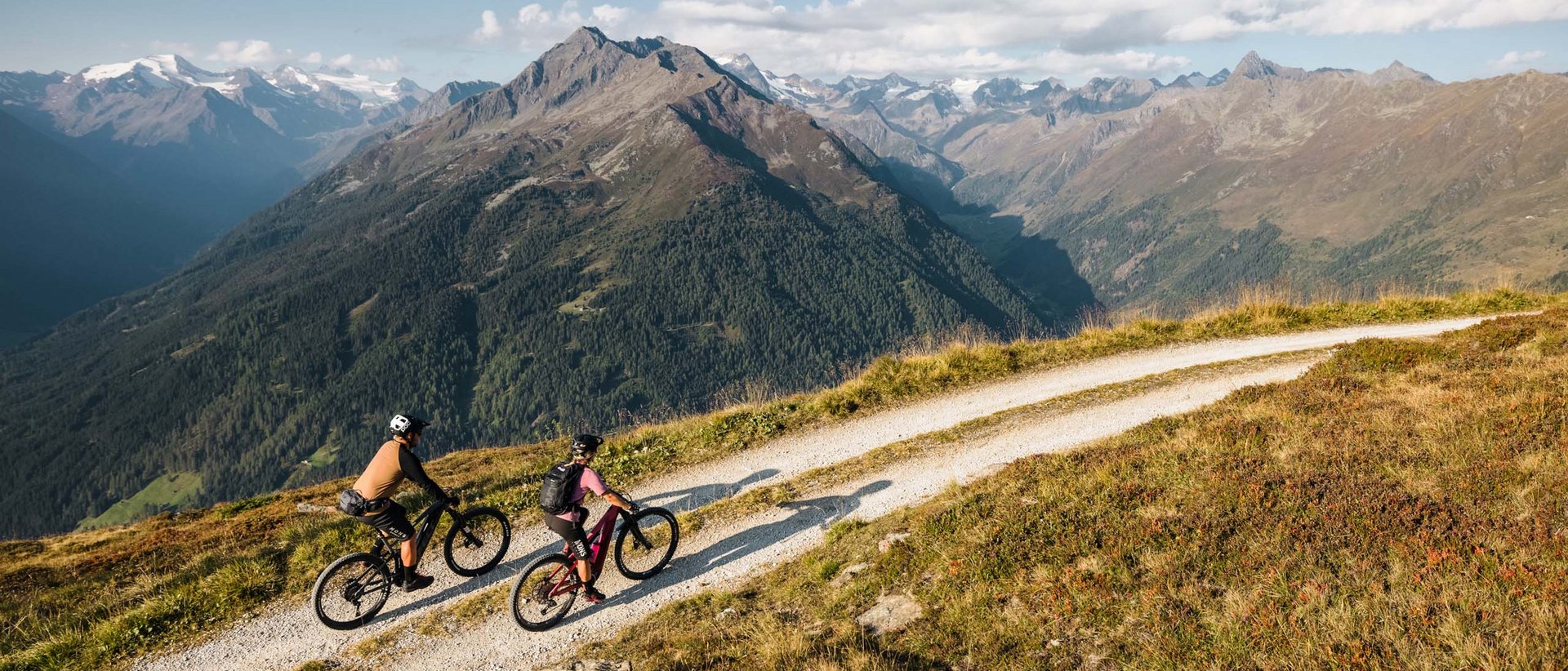 Die schönsten Touren Zwei Mountainbiker fahren auf einem Bergweg mit Alpenpanorama