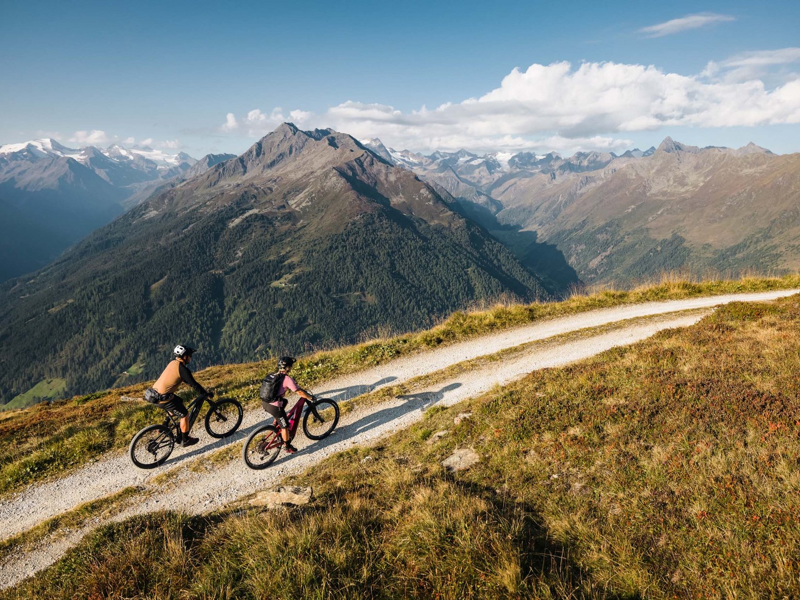 Stubaital: our hotel with a pool Two mountain bikers on a trail with a panoramic view of the Alps