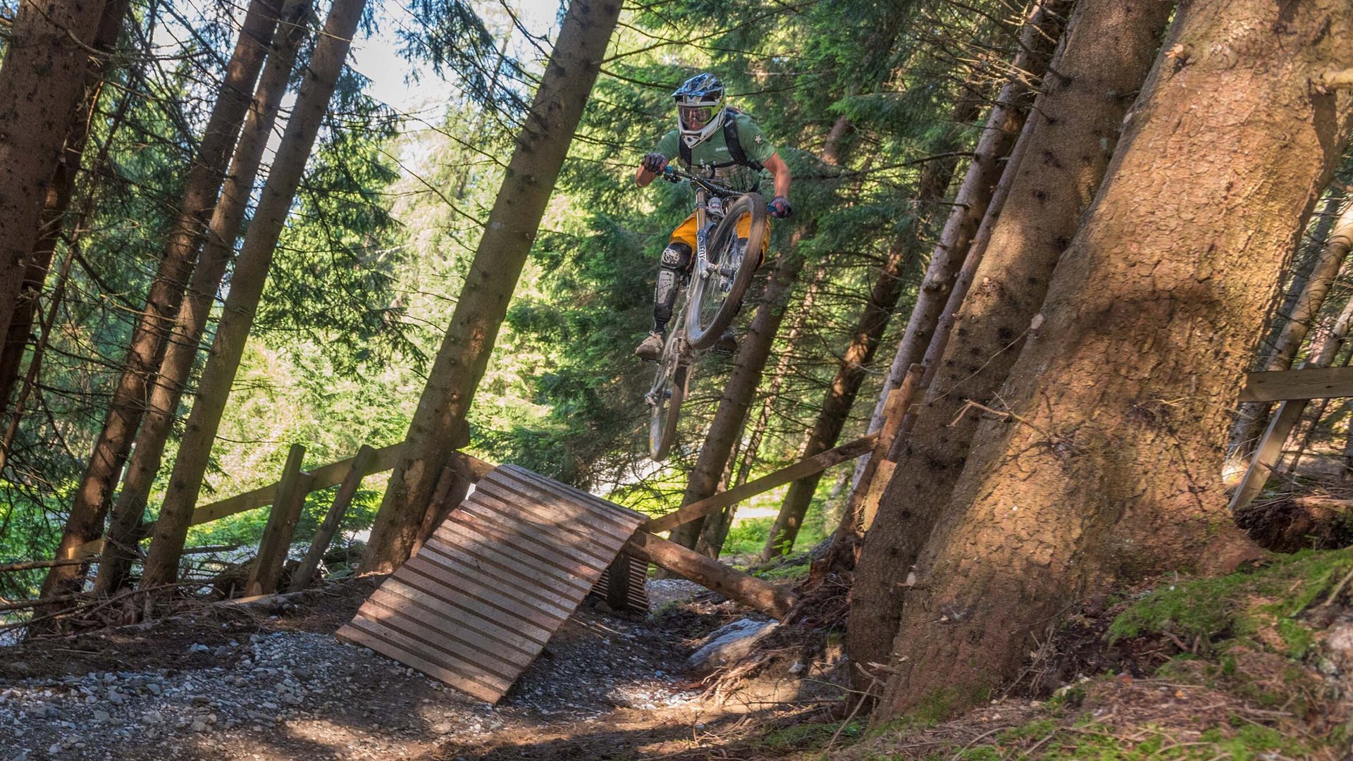 Stubaital: Hiking in summer Mountain biker with helmet jumping off a wooden ramp in forest