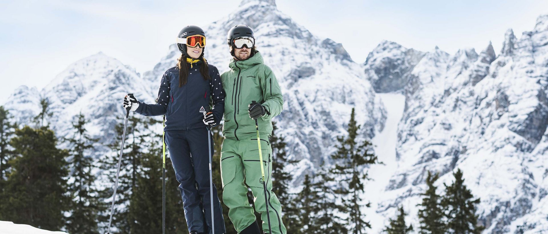 Die Weihnachtszeit bei uns Paar in Skiausrüstung vor verschneiter Berglandschaft und Tannenbäumen