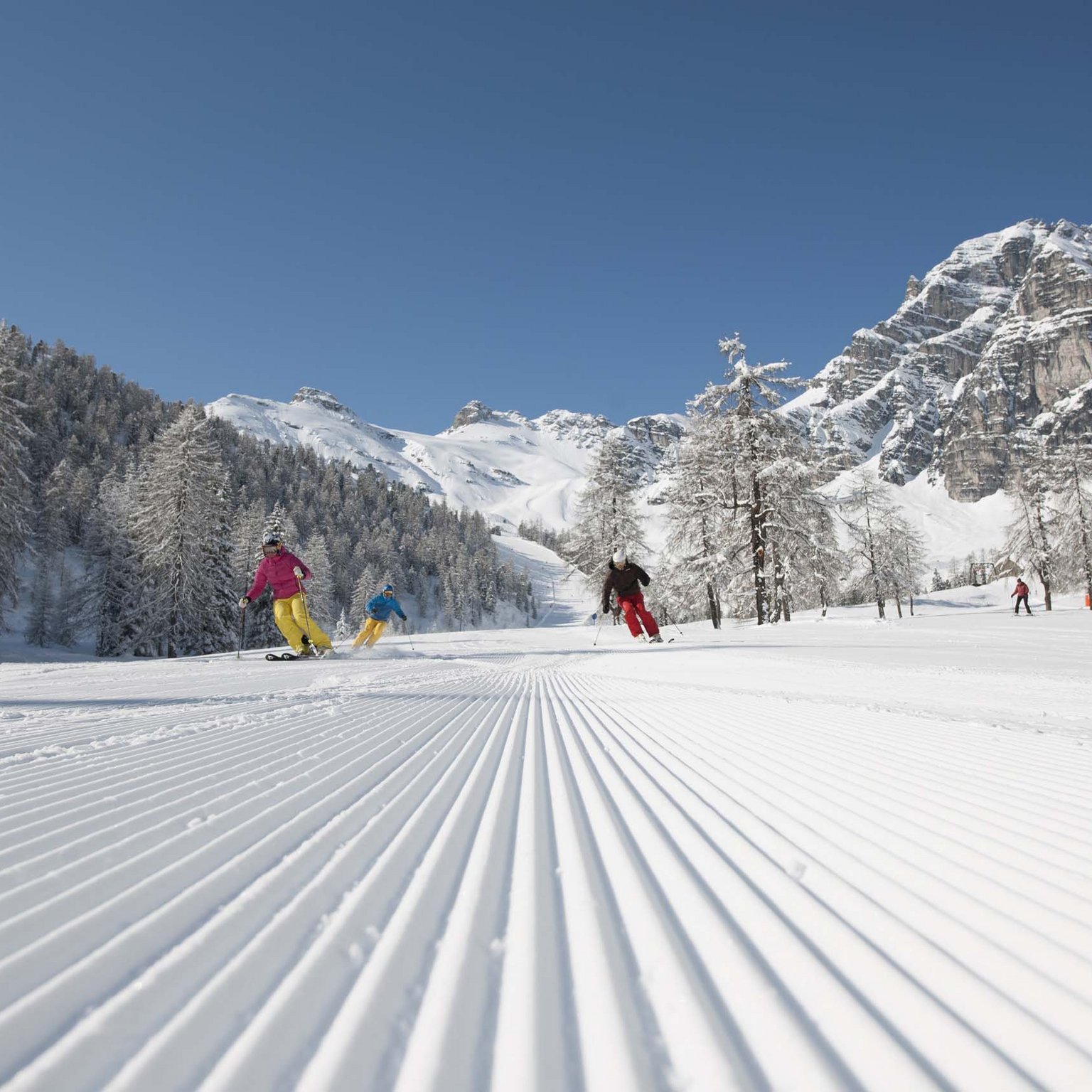 Ecco il nostro hotel: lo Stubai vi aspetta Sciatori su pista battuta con montagne e alberi innevati sullo sfondo