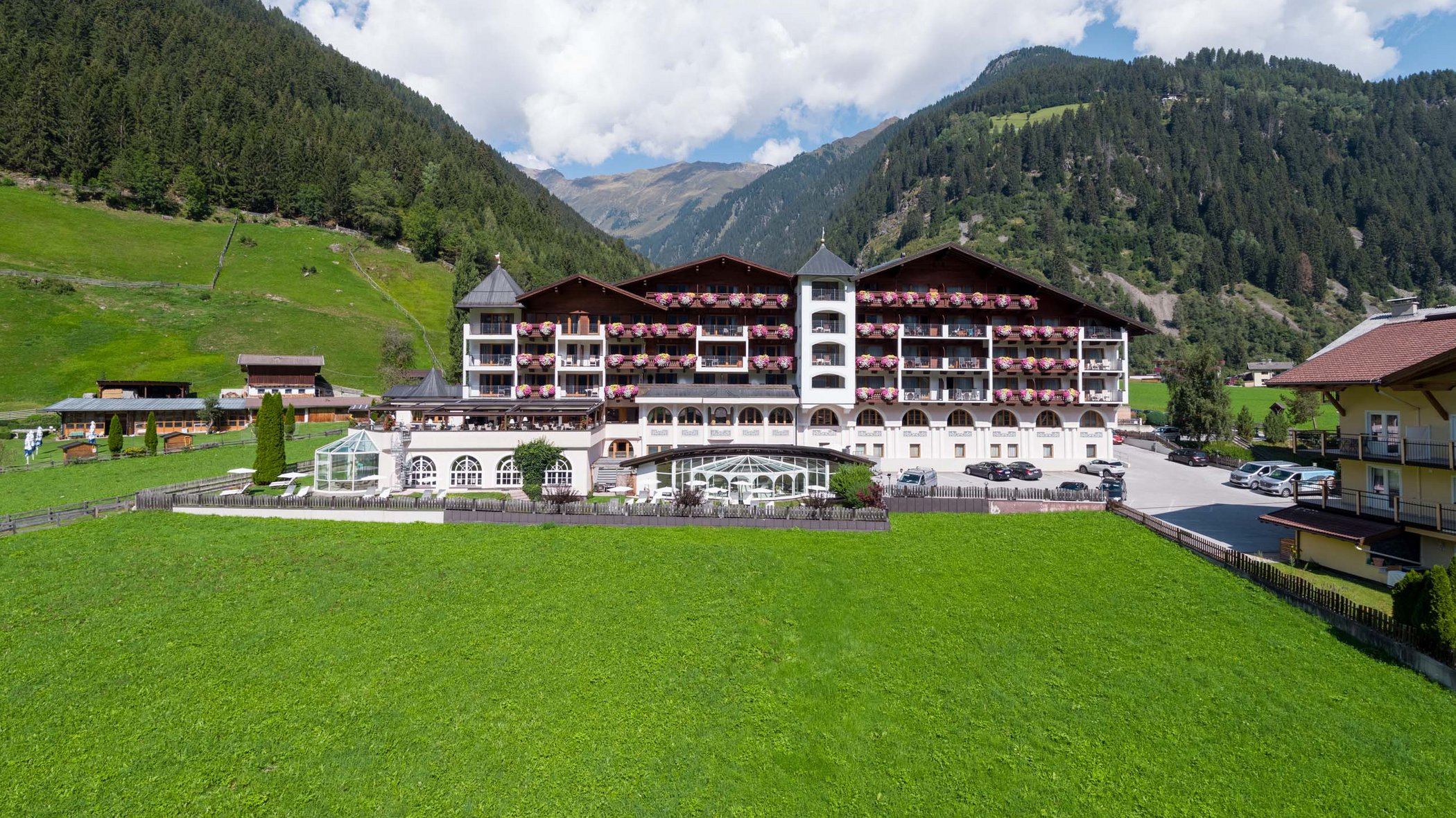 Ecco il nostro hotel: lo Stubai vi aspetta Hotel in un paesaggio montano verde con cielo blu e nuvole bianche