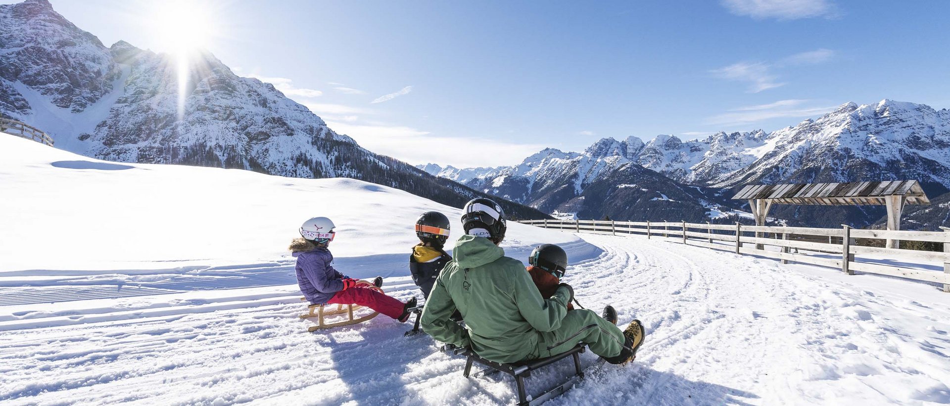 Los geht die Gaudi! Personen rodeln auf schneebedecktem Weg in sonniger Berglandschaft
