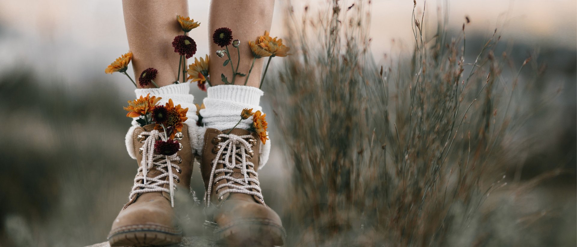 7 typische Fehler beim Wandern – und wie Sie diese vermeiden können Beine mit geschlossenen braunen Stiefeln und Blumen, die aus weißen Socken wachsen