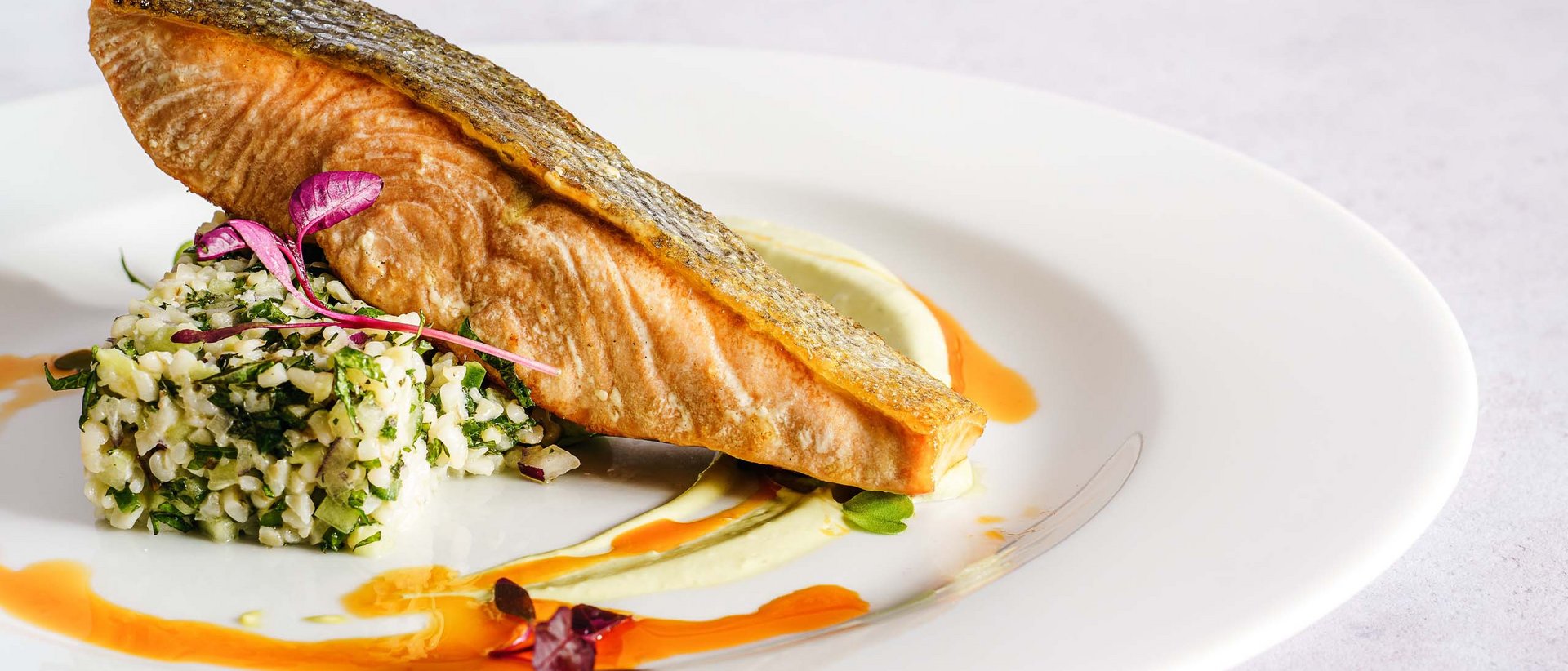 Gaumenfreuden im Milderer Hof Gebratenes Lachsfilet mit Kräuterreis und Soßendekoration auf weißem Teller