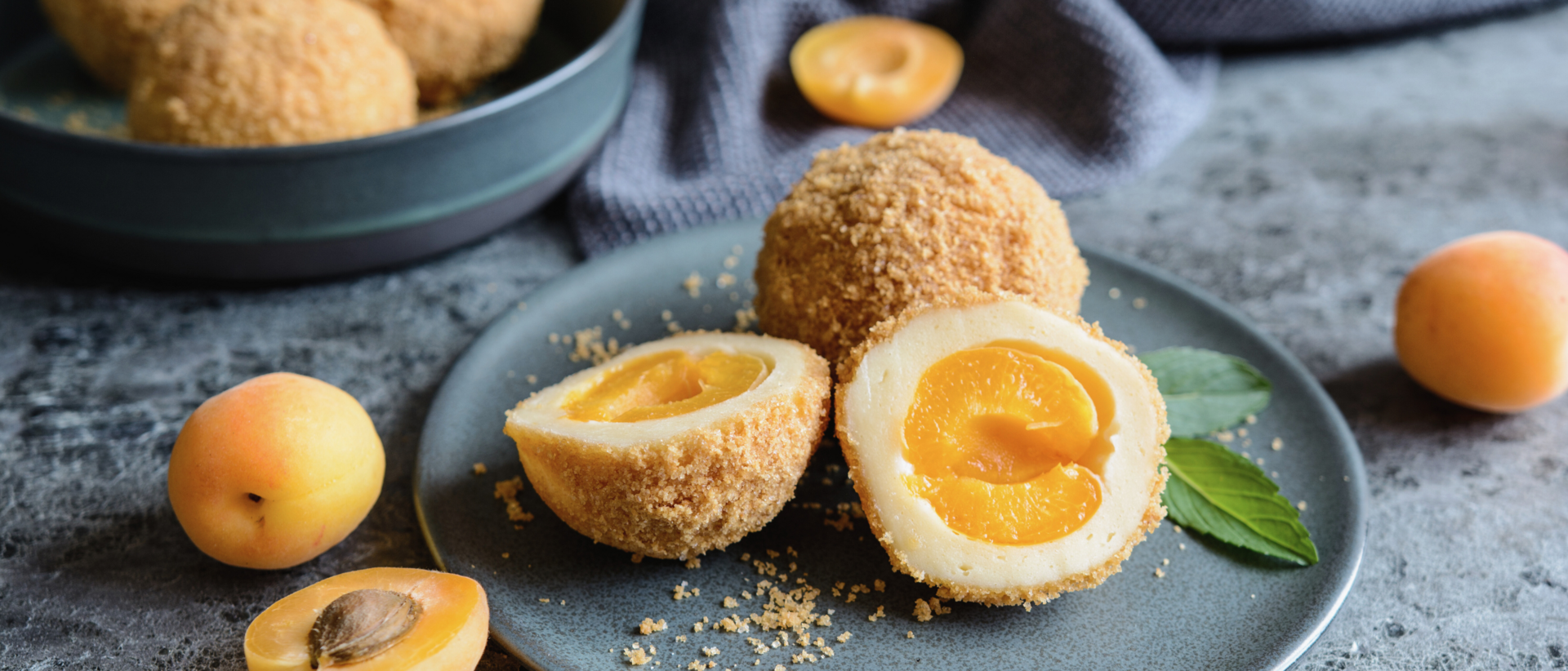 Marillenknödel wie im Urlaub: Unser Rezept aus dem Milderer Hof Marillenknödel mit Marillen auf einem Teller und Schüssel im Hintergrund