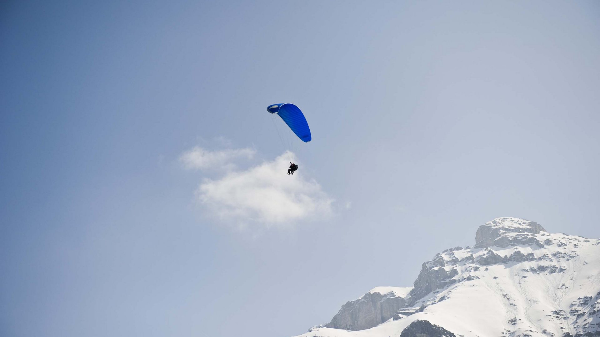 Things to do in Stubaital Paraglider with blue wing flying over snowy mountain under clear sky
